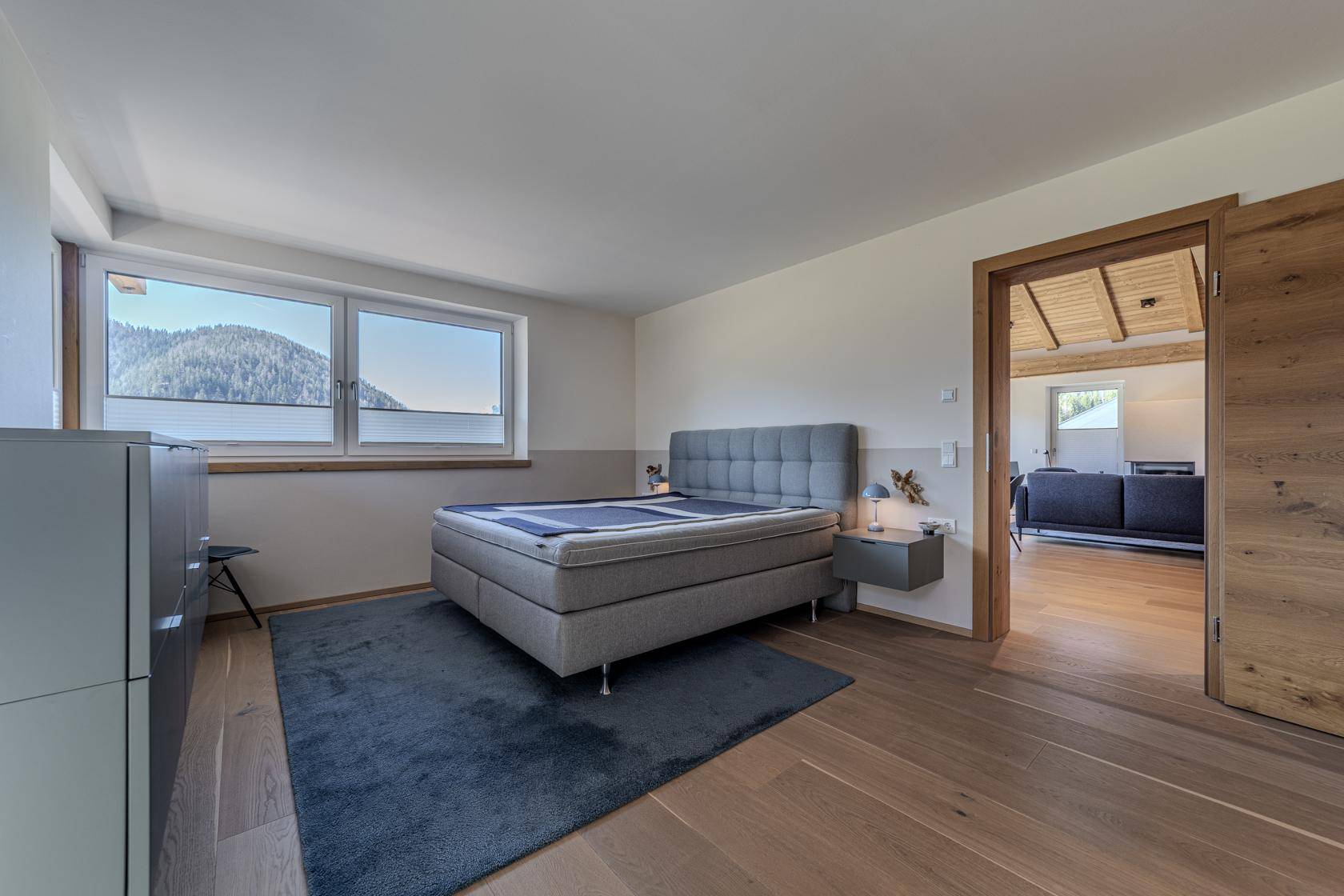 Helles Schlafzimmer mit komfortablem Bett, Holzboden und Fenster mit Bergblick.
