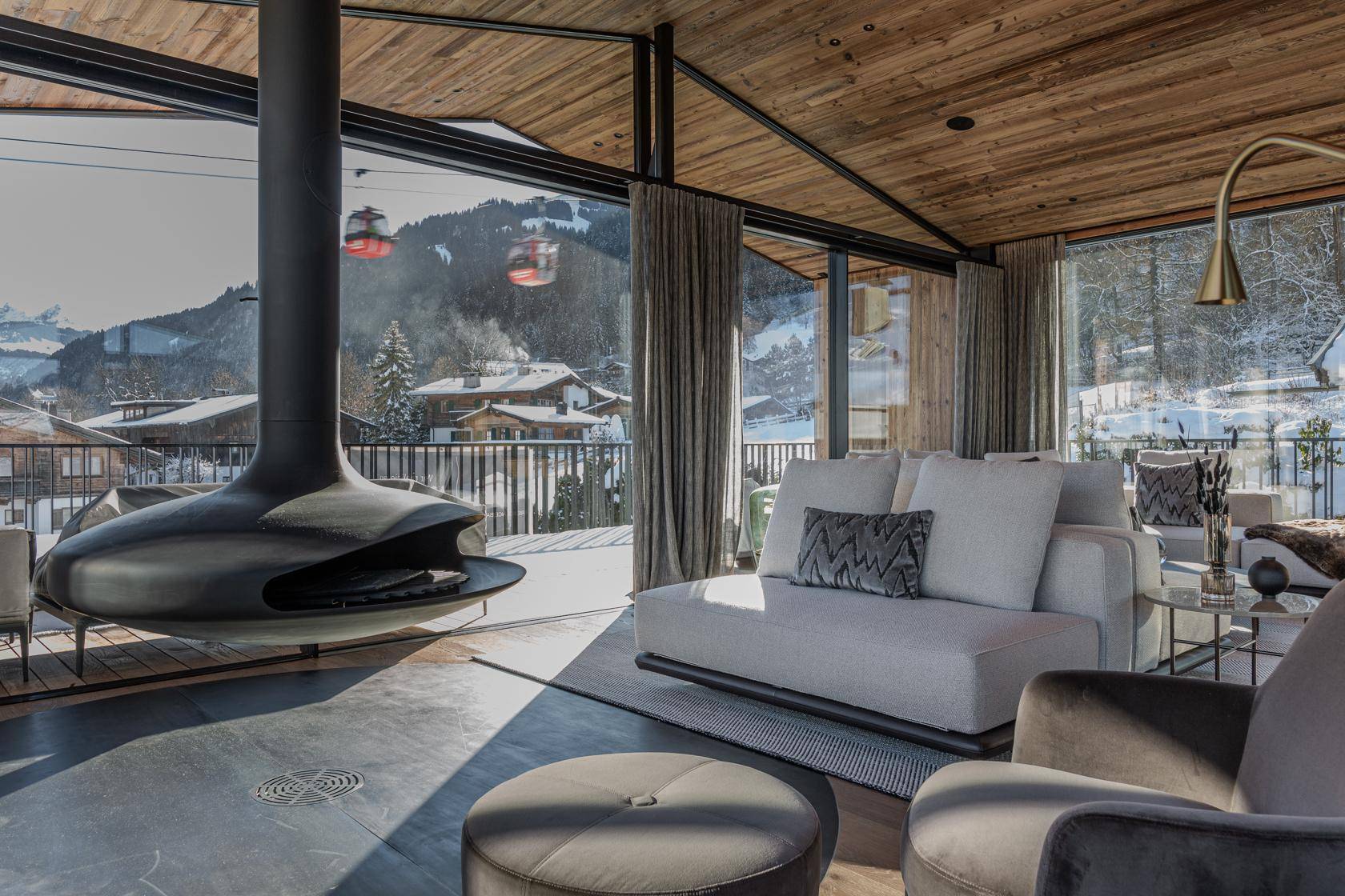 Helles Wohnzimmer mit modernem Kamin, bequemen Sofas und Blick auf die verschneite Landschaft und Skilifte.