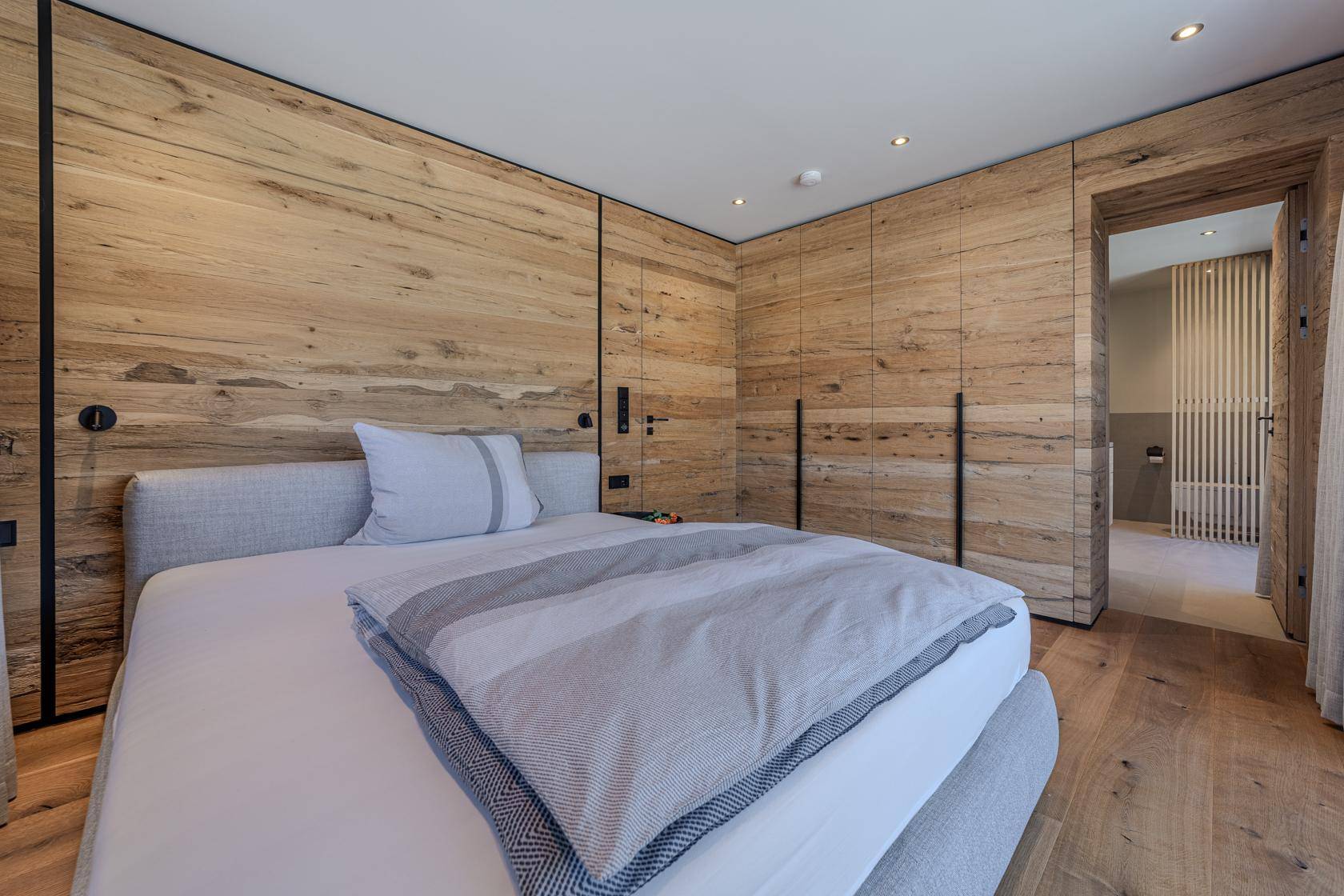 Modernes Schlafzimmer mit Holzwänden, Einbauschränken und Zugang zum Badezimmer.