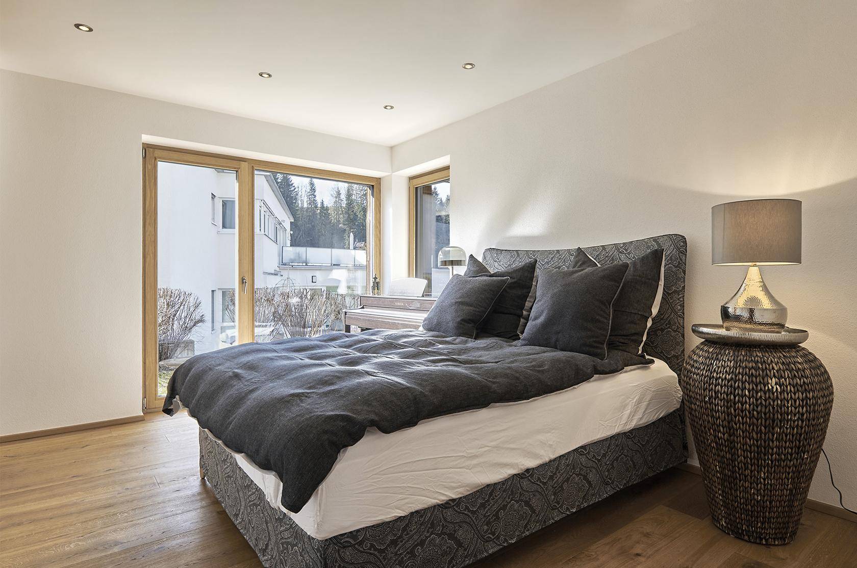 Helles Schlafzimmer mit großem Bett, Holzboden und weitem Blick durch die Fenster.