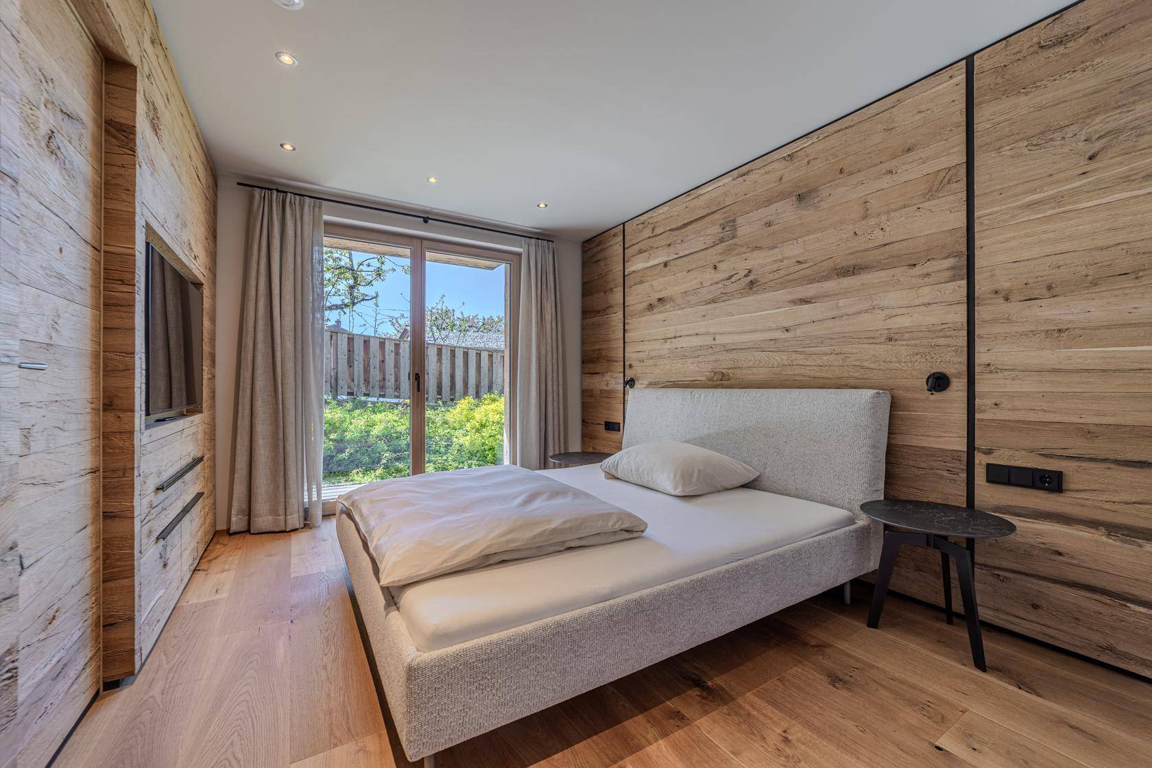Schlafzimmer mit Holzboden und Zugang zum Garten, umgeben von grüner Natur.