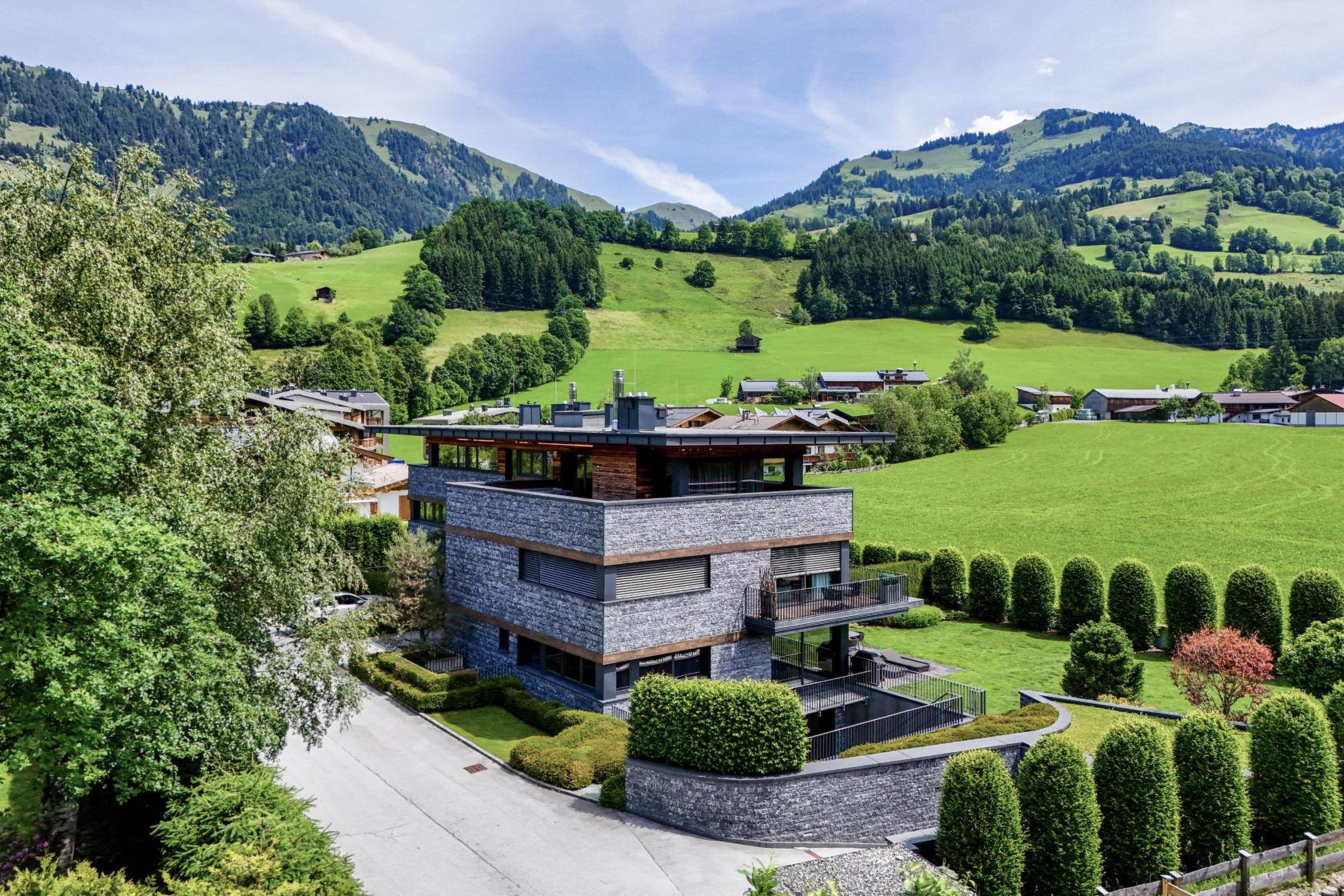 Architektonisch anspruchsvolle Villa in alpiner Landschaft, umgeben von grünen Hügeln und Panoramablick.