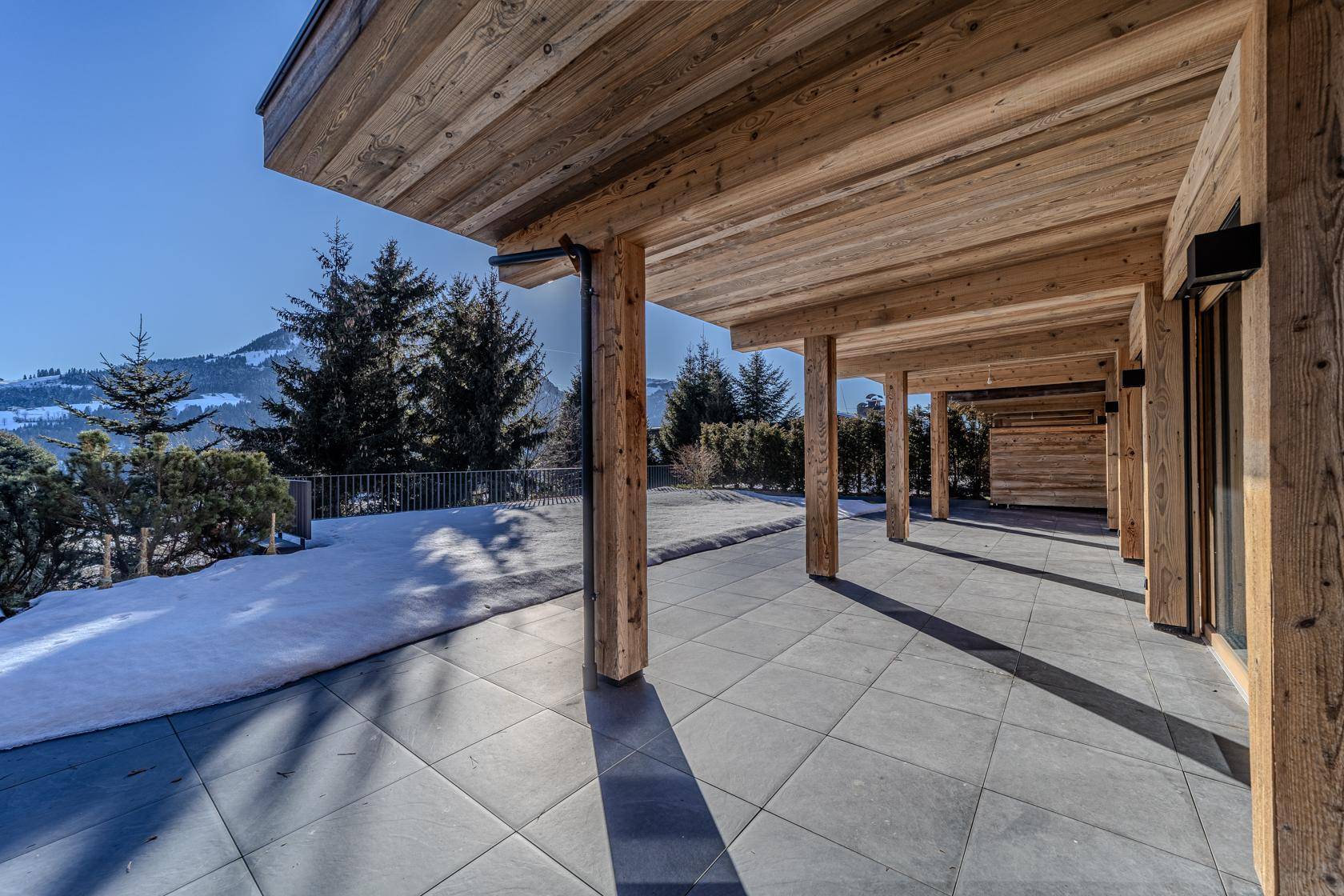 Geräumige, überdachte Terrasse mit Holzbalken und Panoramablick auf die Alpenlandschaft.