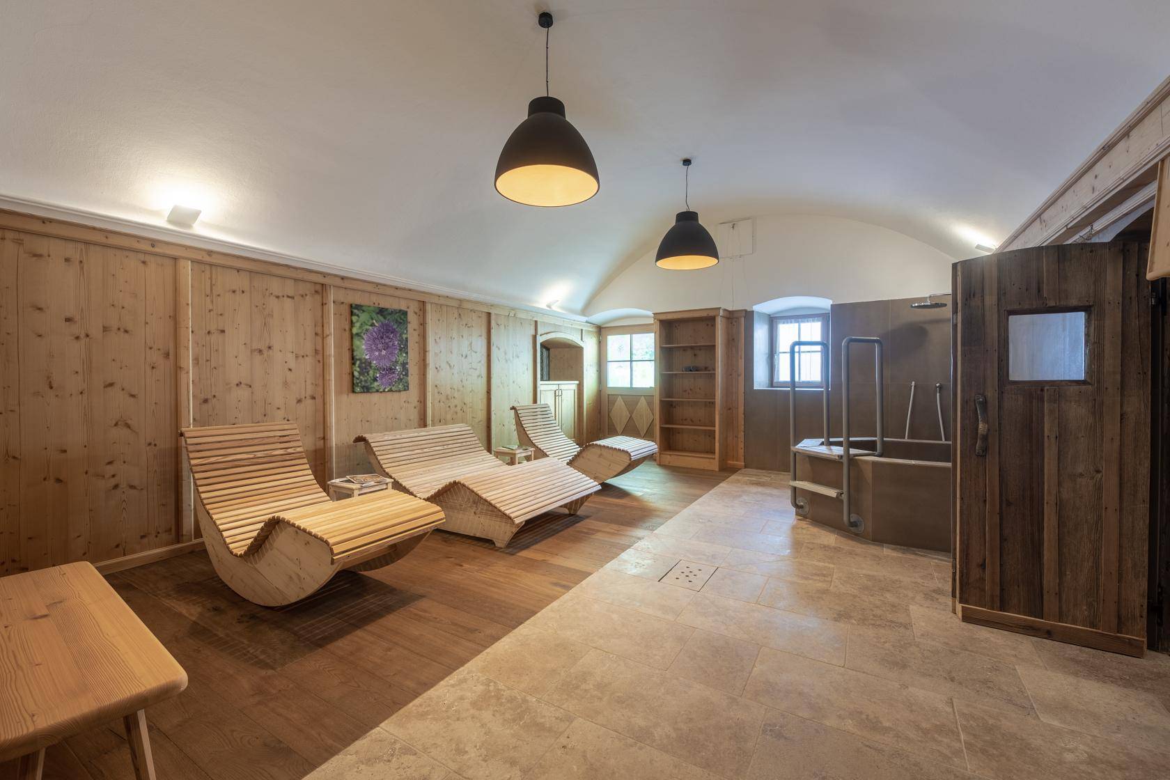 Entspannungsbereich mit Holzliegen, Fliesenboden und Zugang zur Sauna.
