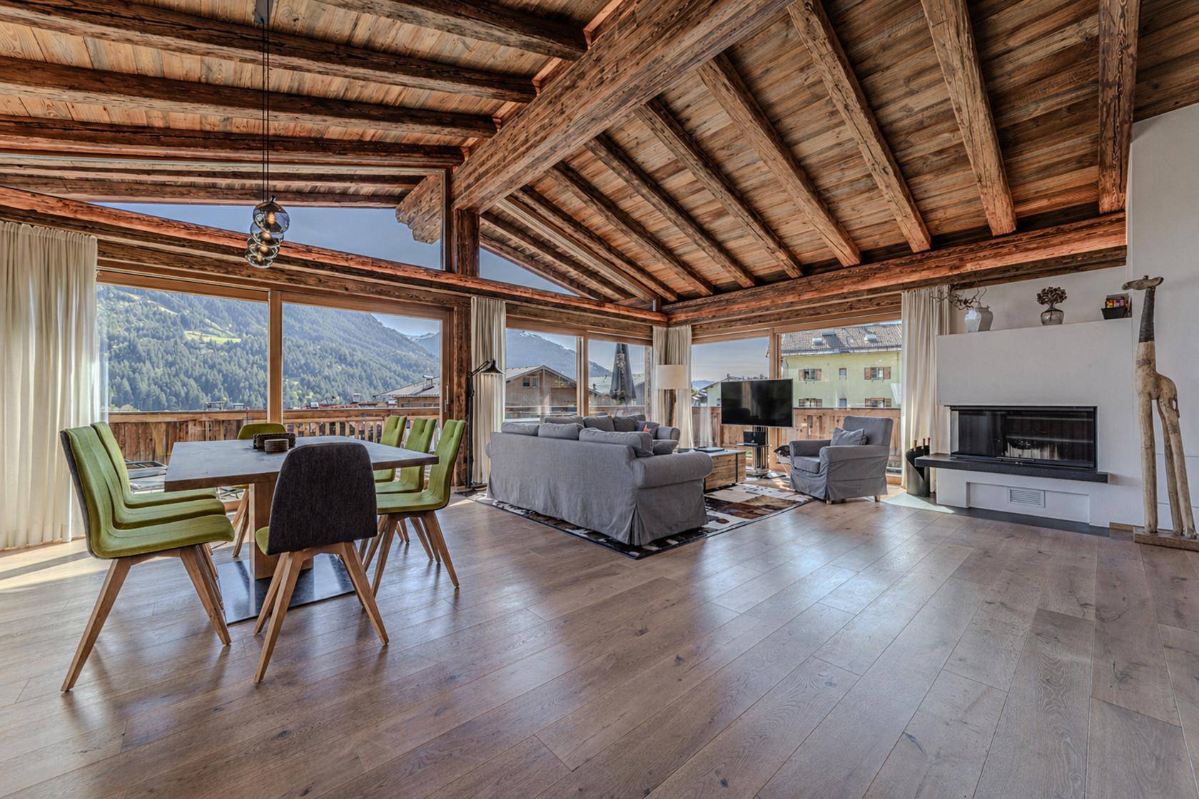Heller Wohn-Essbereich mit Holzbalken, Kamin und weitem Blick auf die Berge.