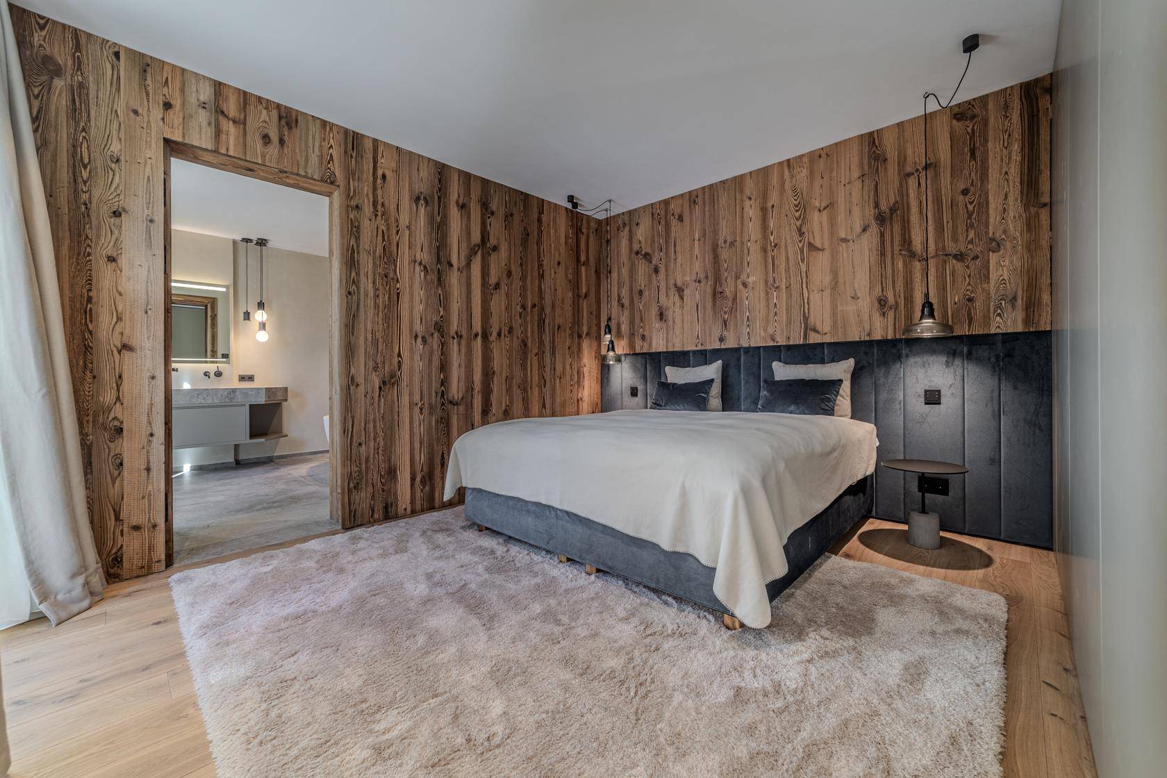 Gemütliches Schlafzimmer mit Holzwänden, großem Bett und offenem Zugang zum Badezimmer.