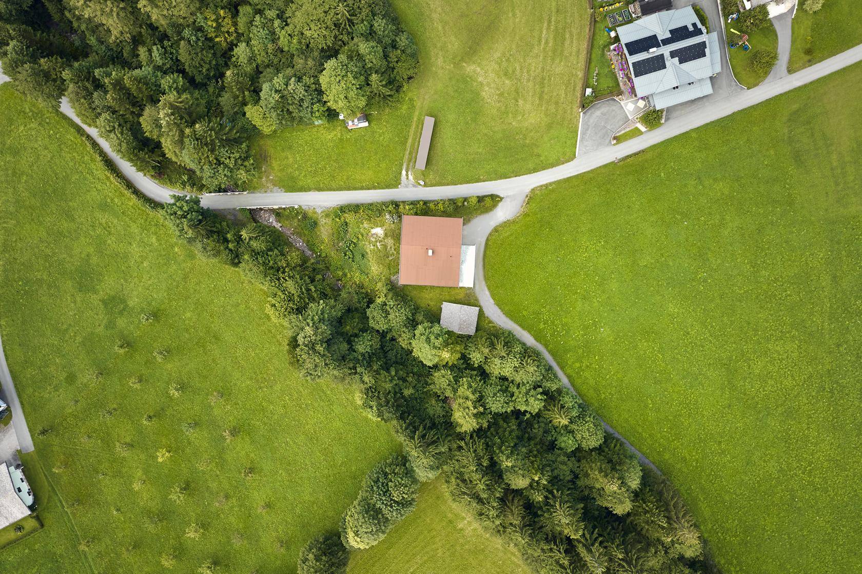 Luftaufnahme eines Hauses inmitten weitläufiger grüner Felder und kleiner Waldstücke.
