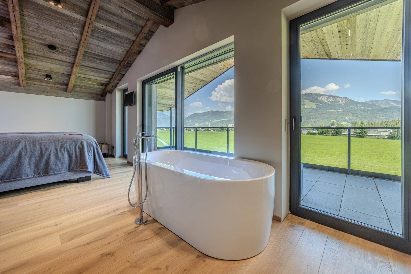 Helles Schlafzimmer mit freistehender Badewanne und großen Fenstern, die einen weiten Bergblick bieten.