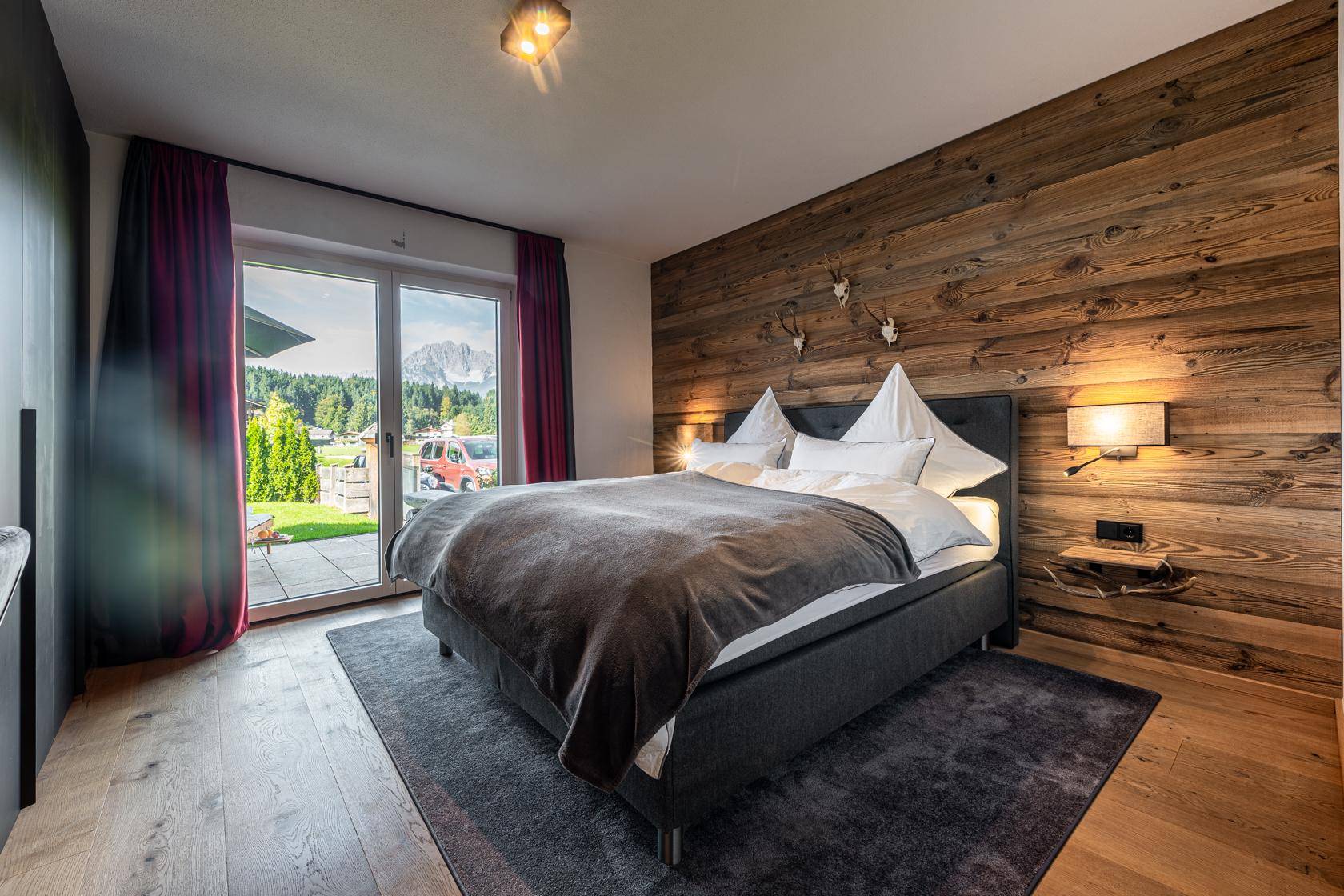 Helles Schlafzimmer mit Holzwand, Doppelbett und direktem Zugang zum Garten.
