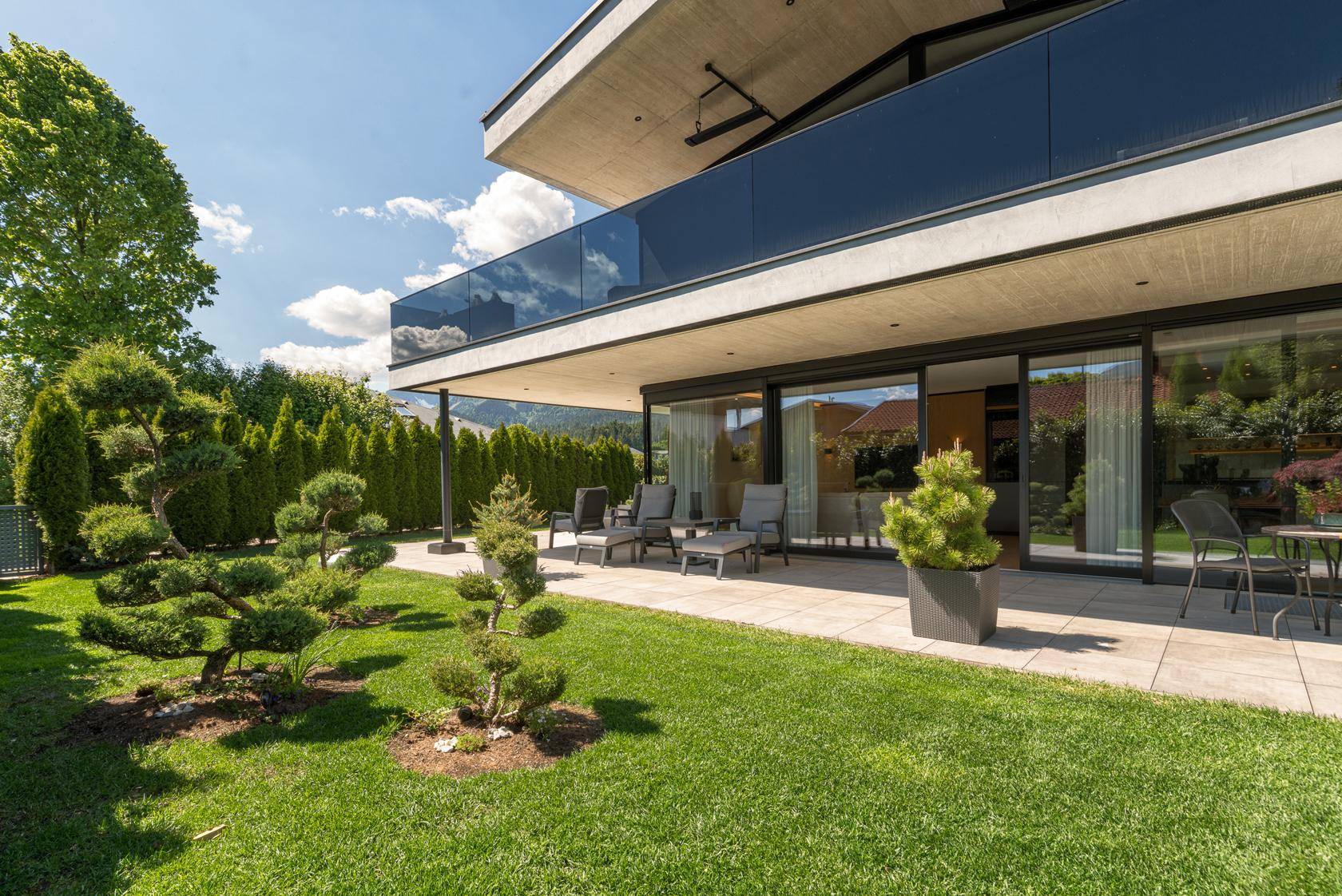 Gepflegter Garten mit Terrasse, Zierbäumen und moderner Architektur im Hintergrund.