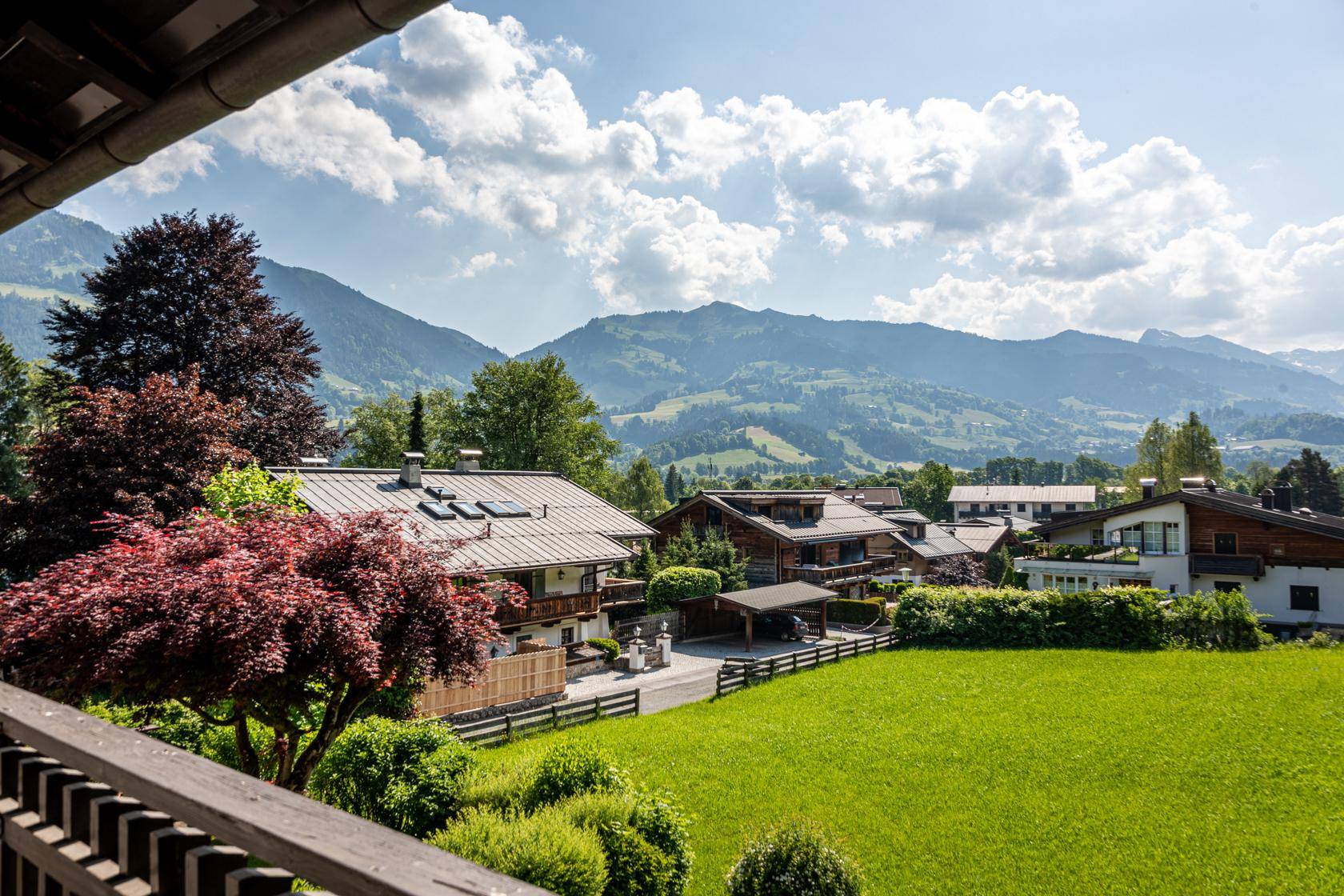 Blick vom Balkon auf die idyllische Nachbarschaft, grüne Wiesen und die majestätischen Berge.