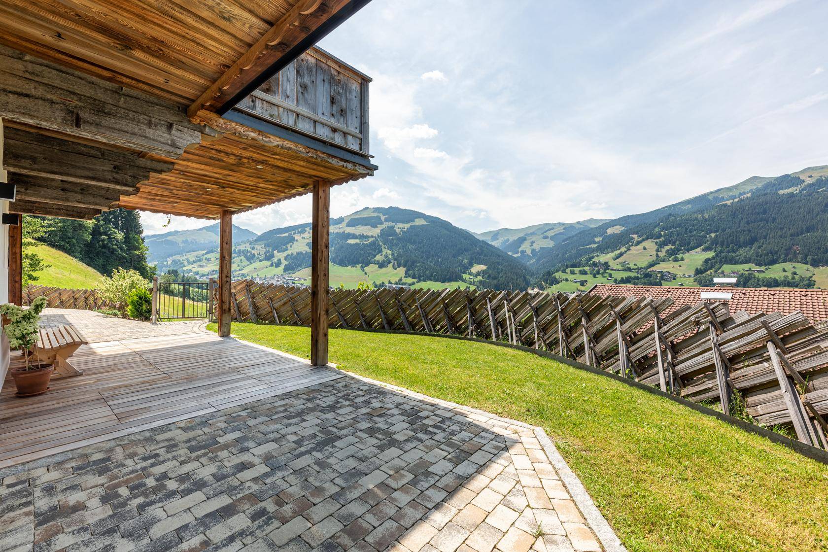 Überdachte Terrasse mit Holzboden und gepflastertem Bereich, umgeben von Natur.
