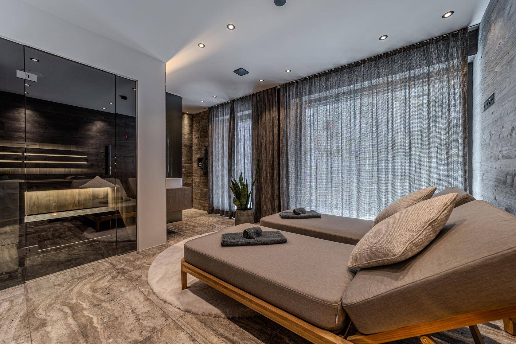 Moderner Wellnessbereich mit Liegen, verglaster Sauna und großen Fenstern für Entspannung.