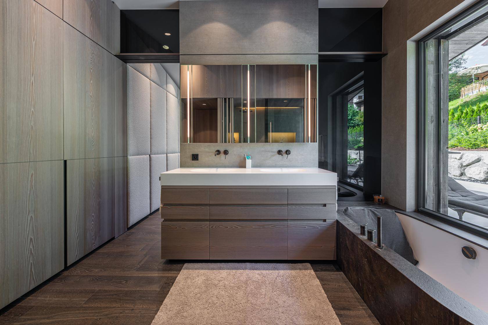 Elegantes Badezimmer mit Doppelwaschbecken, großer Spiegelfront und Badewanne mit Blick ins Grüne.