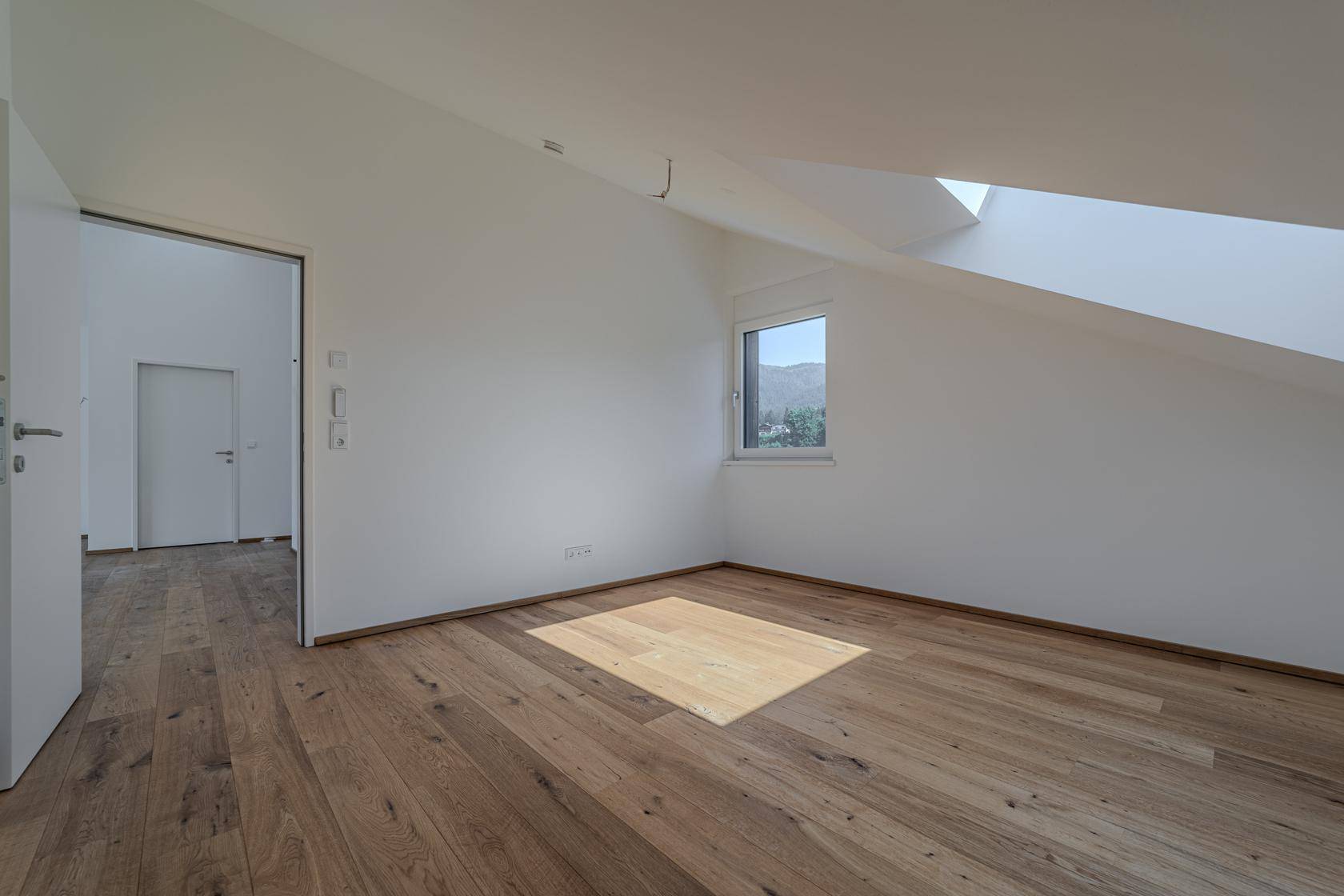 Helles Schlafzimmer mit Holzboden, Dachschräge und Fenster, das viel Tageslicht hereinlässt.