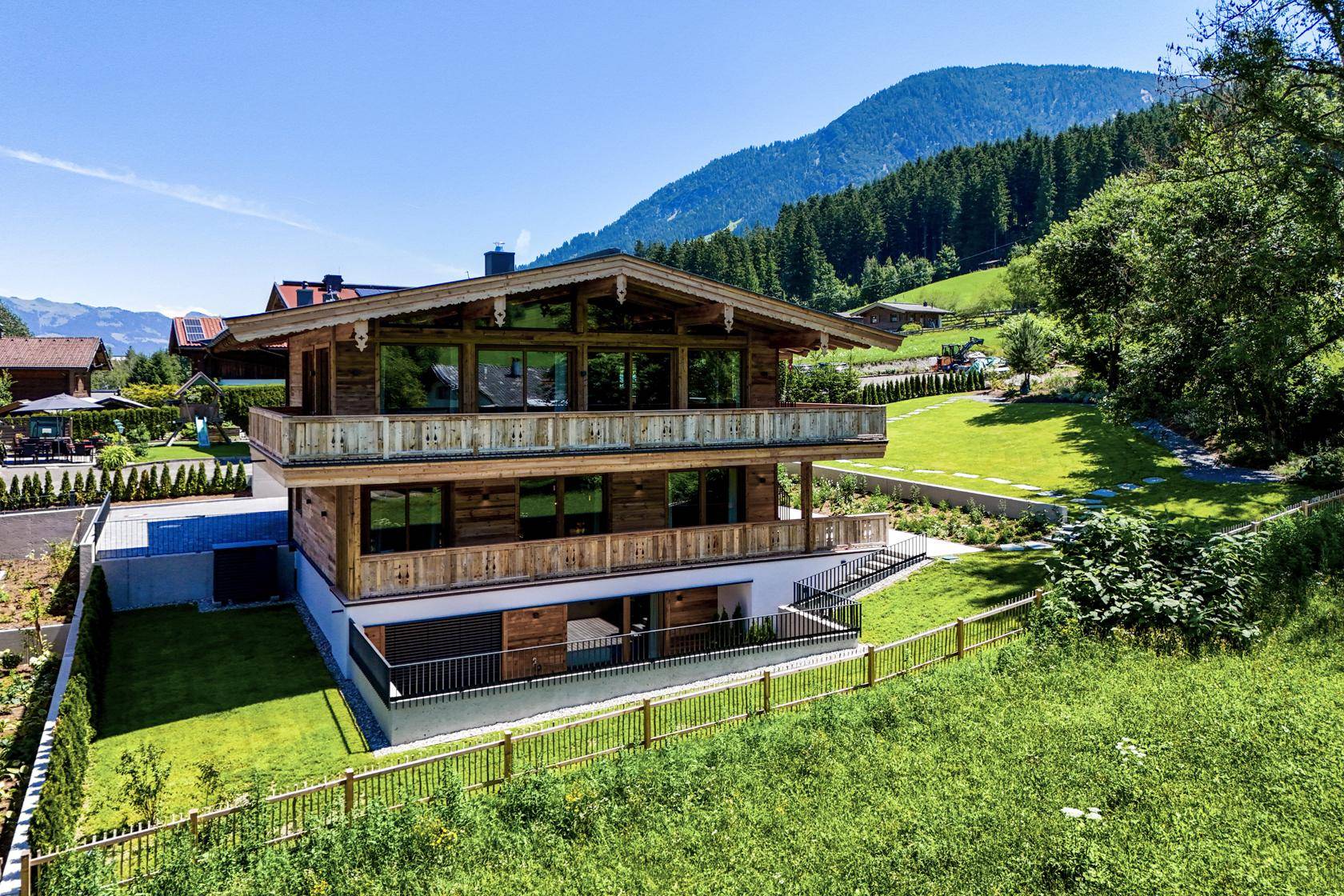 Exklusives Chalet mit Holzfassade, mehreren Balkonen und Panoramablick auf die Berge und grüne Landschaft.
