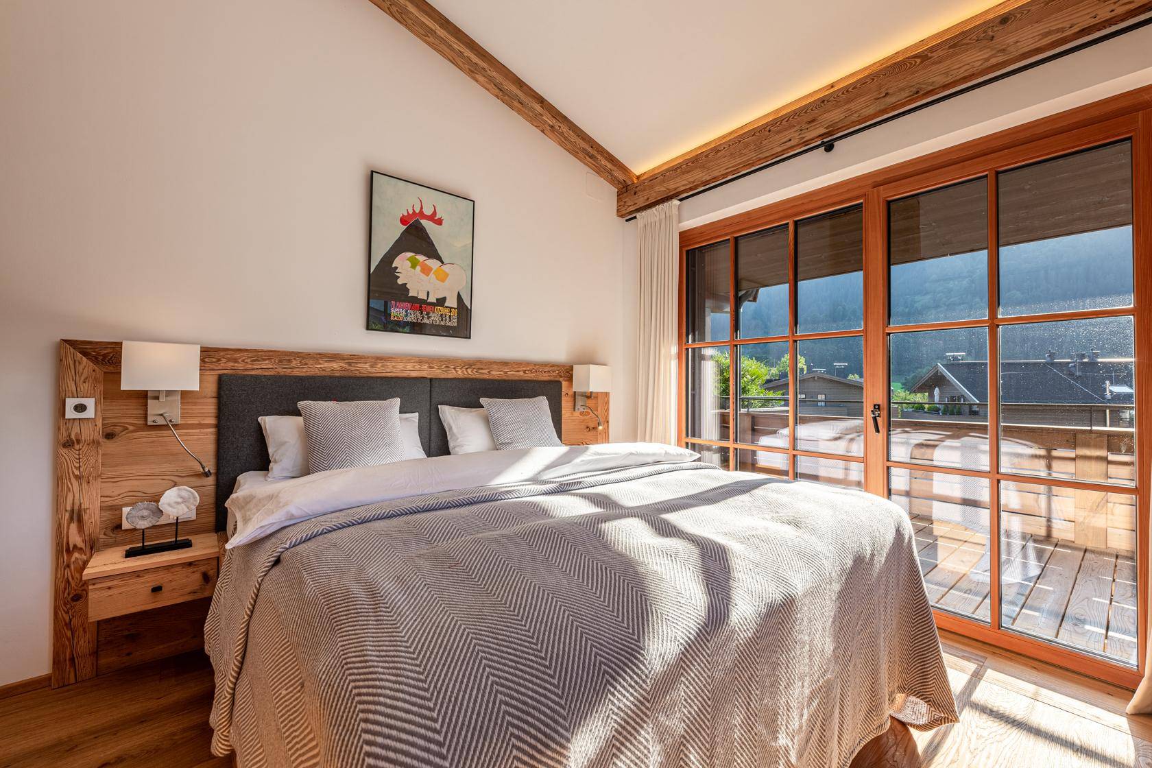 Helles Schlafzimmer mit Holzboden, Balkonzugang und weitem Blick auf die Berglandschaft.