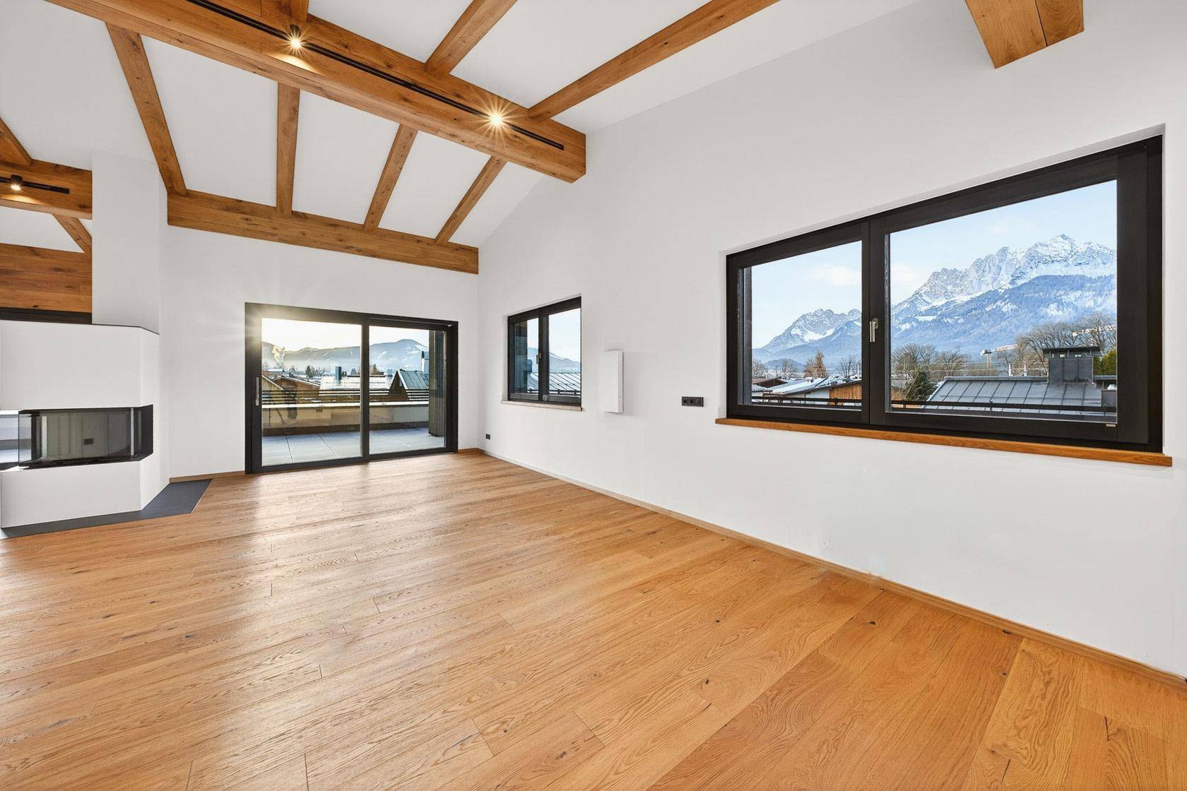 Heller Wohnbereich mit Holzbalkendecke, Eichenparkett und großen Fenstern mit Bergblick.