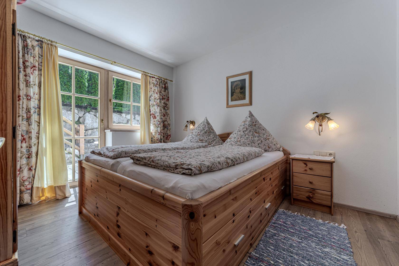 Helles Schlafzimmer mit Doppelbett aus Holz und direktem Zugang zum Gartenbereich.