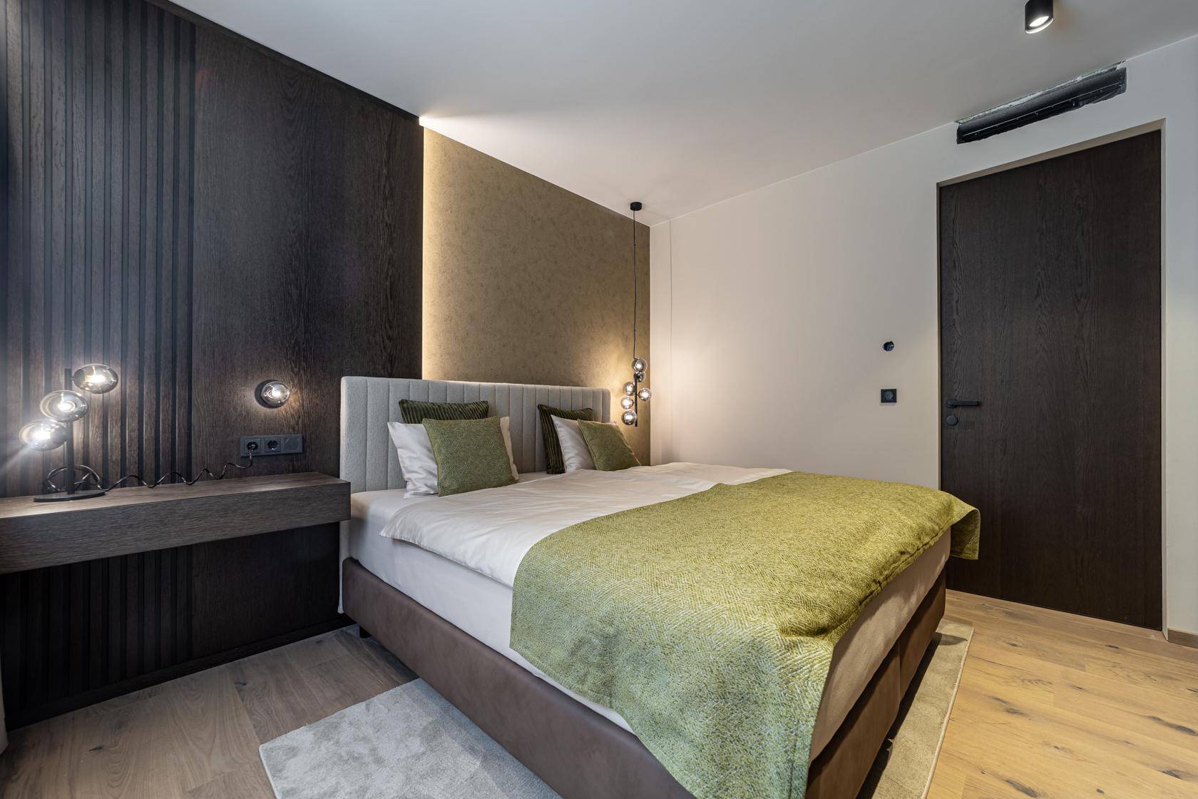 Modernes Schlafzimmer mit großem Bett, Holzboden und stilvoller Wandverkleidung mit indirekter Beleuchtung.