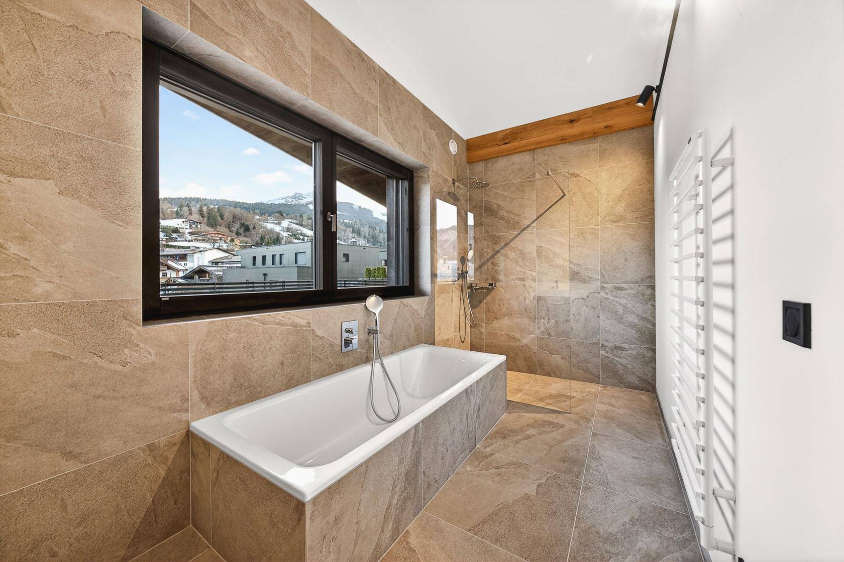 Modernes Badezimmer mit großer Badewanne, Fliesenboden und Fenster mit Blick auf die verschneite Berglandschaft.