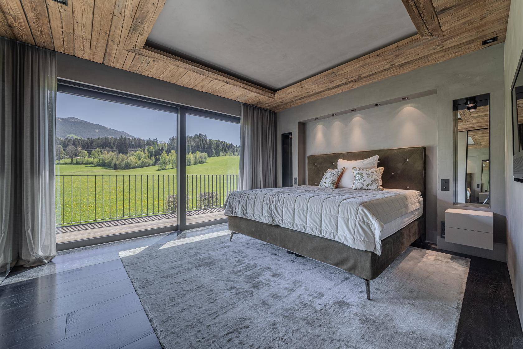Helles Schlafzimmer mit Holzakzenten, großem Bett und Balkonzugang mit Bergblick.