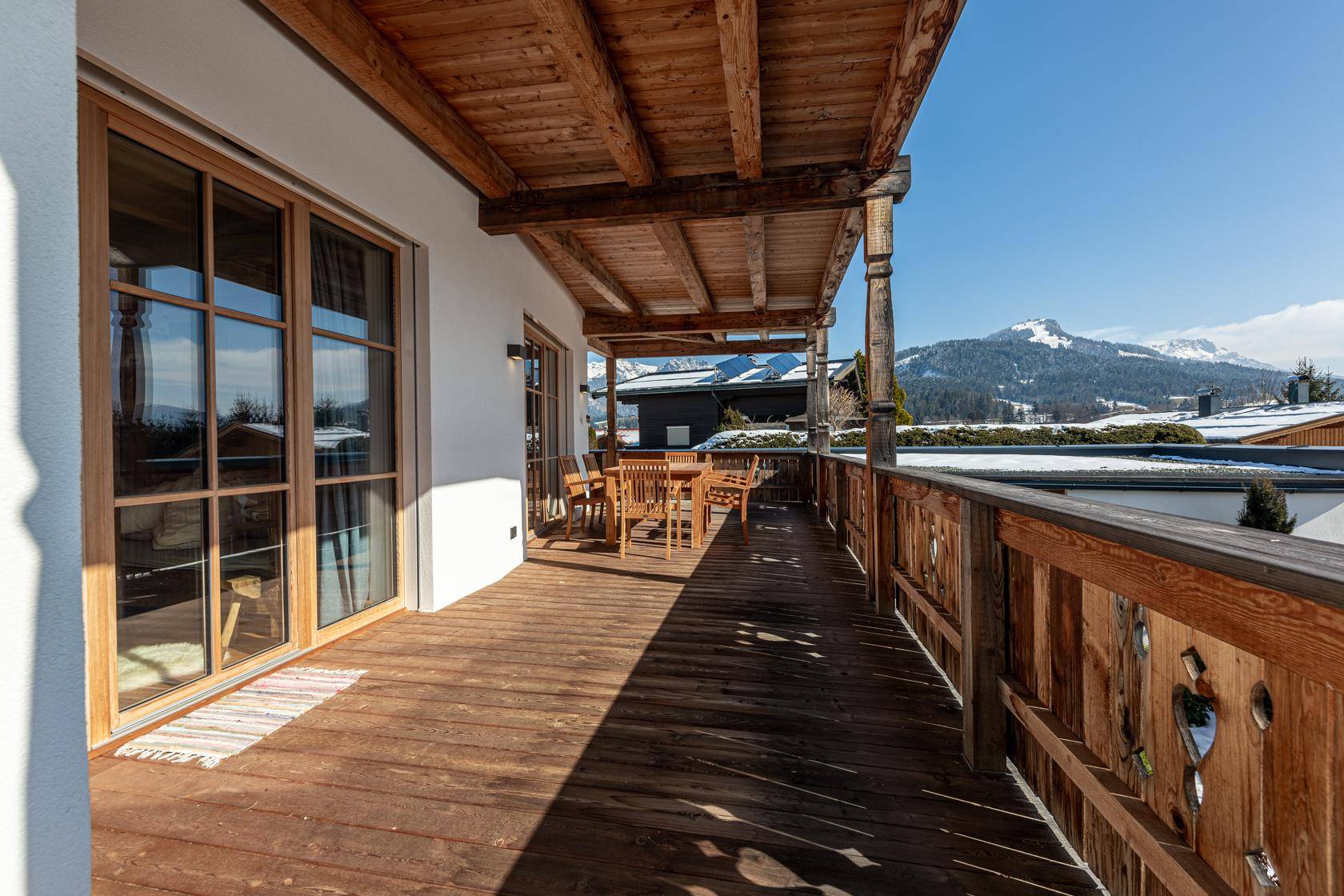 Großer Holzbalkon mit Essbereich und weitem Blick auf die verschneite Berglandschaft.