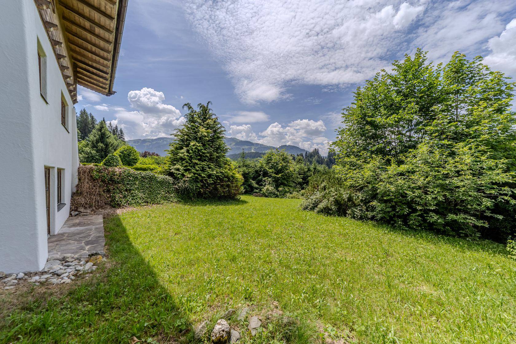 Seitlicher Gartenbereich mit Steinfliesen und weitem Blick auf die grüne Berglandschaft.