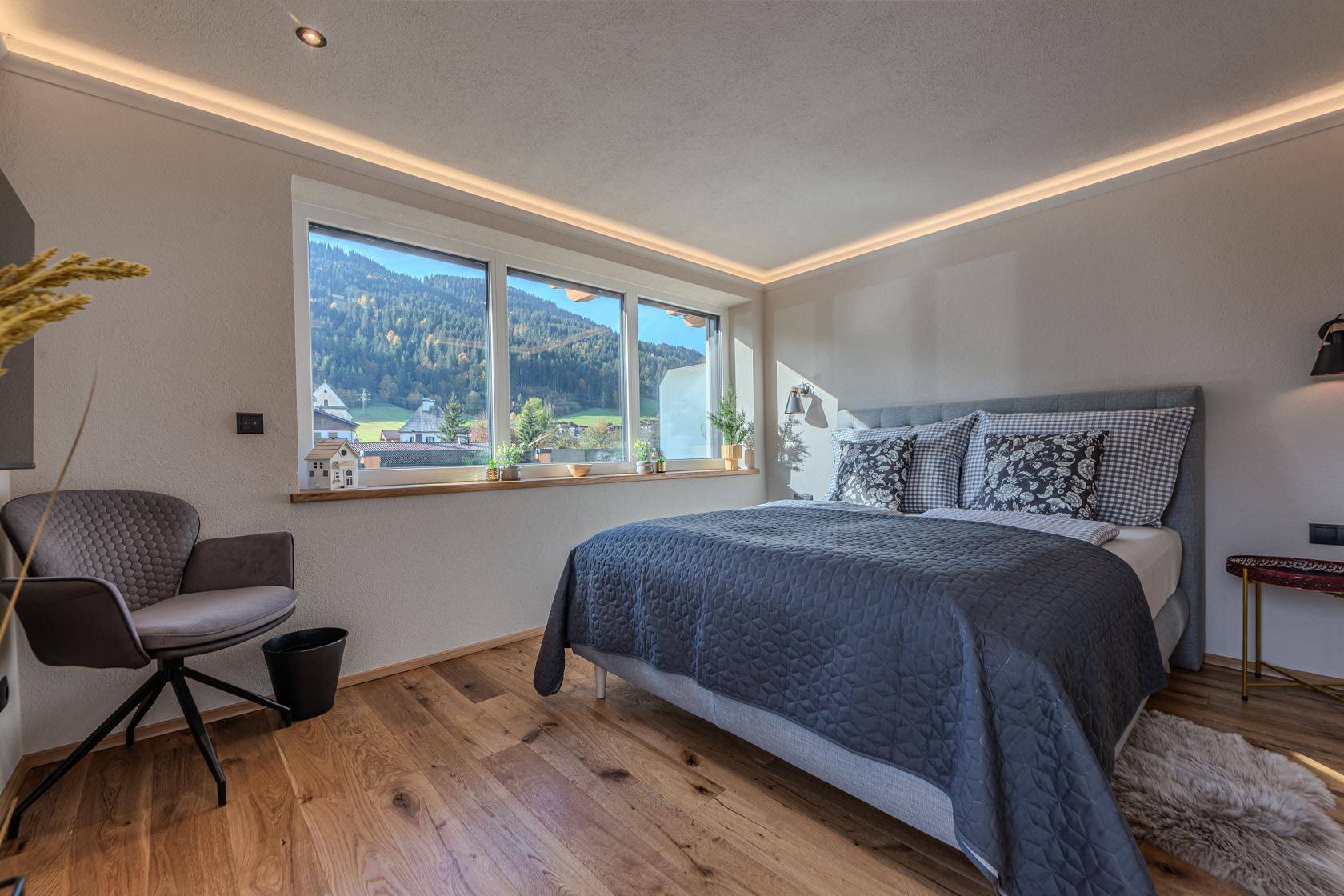Helles Schlafzimmer mit Holzboden, indirekter Beleuchtung und weitem Bergblick.