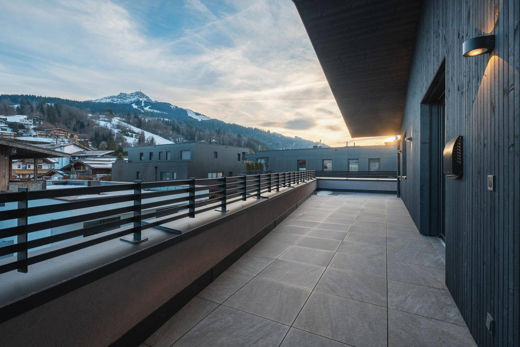 Lange Terrasse mit Fliesenboden und Geländer, die einen weiten Blick auf die Berglandschaft bietet.