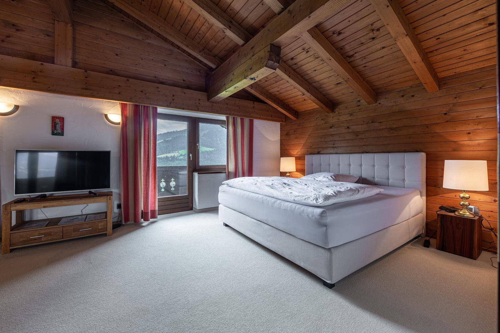 Geräumiges Schlafzimmer mit Holzbalkendecke, Teppichboden und Balkonzugang mit Bergblick.