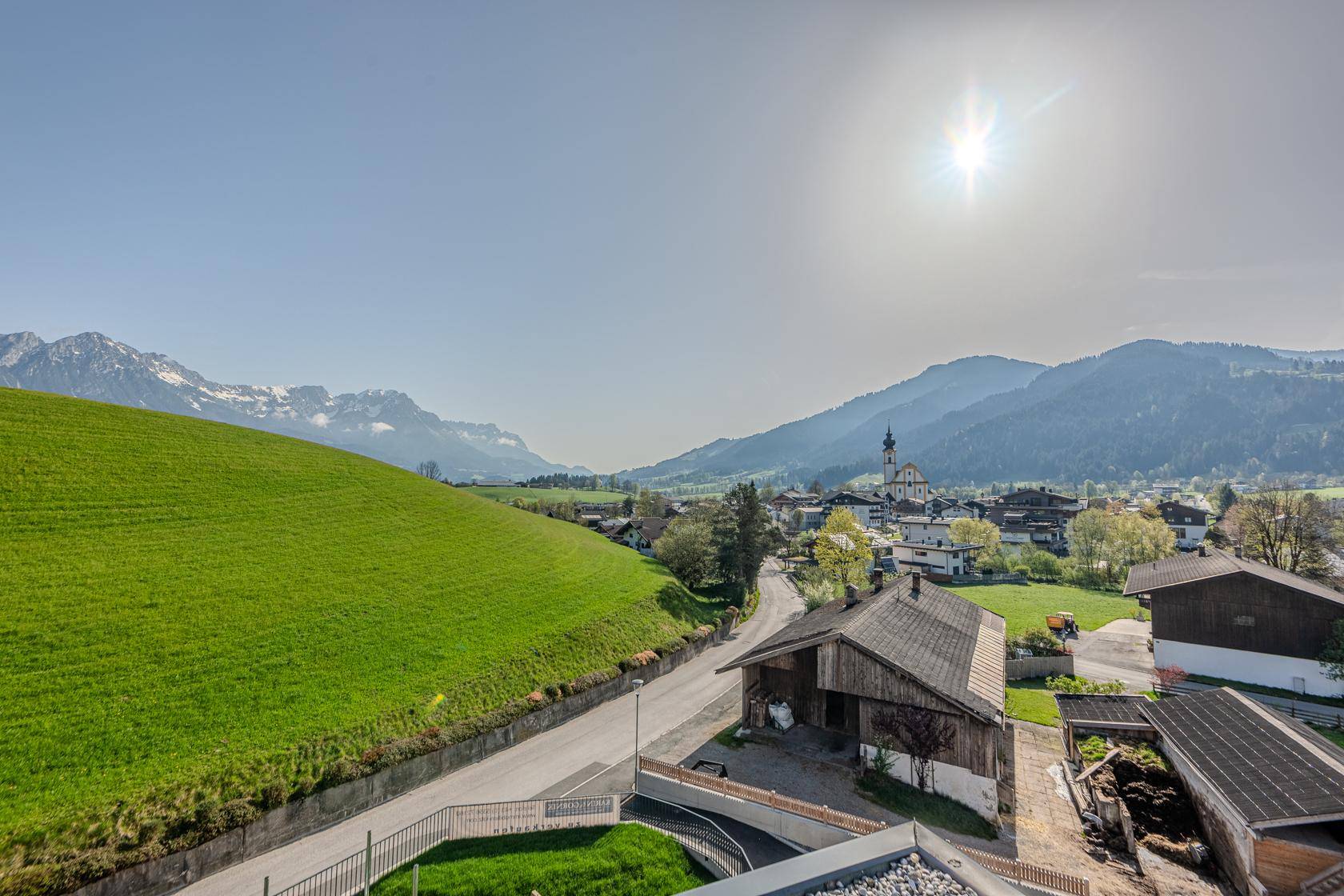 Panoramablick auf ein malerisches Dorf in einem Tal, umgeben von grünen Hügeln und Bergen.