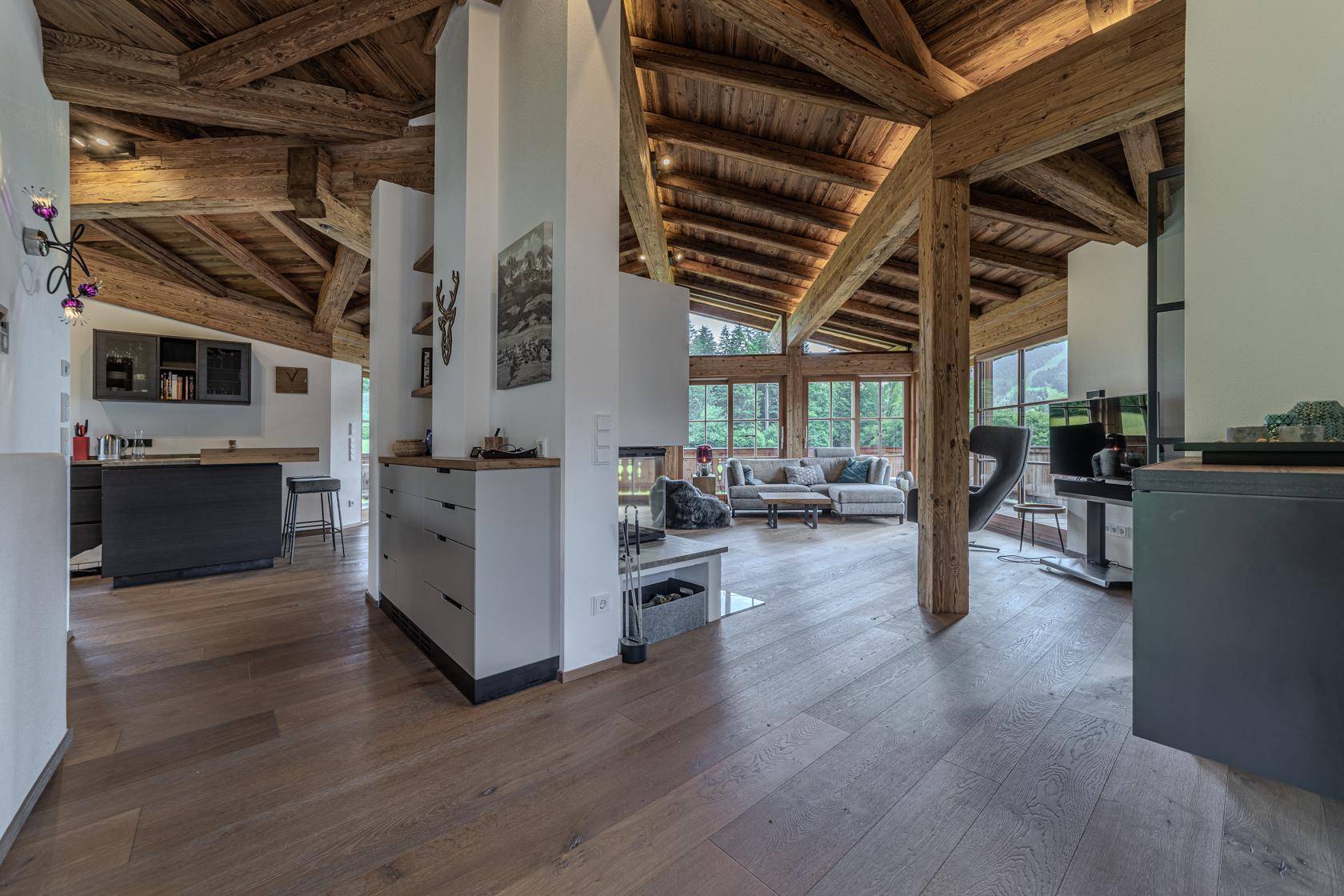 Offener Wohnbereich mit Holzbalkendecke, Kamin und Übergang zur modernen Küche.