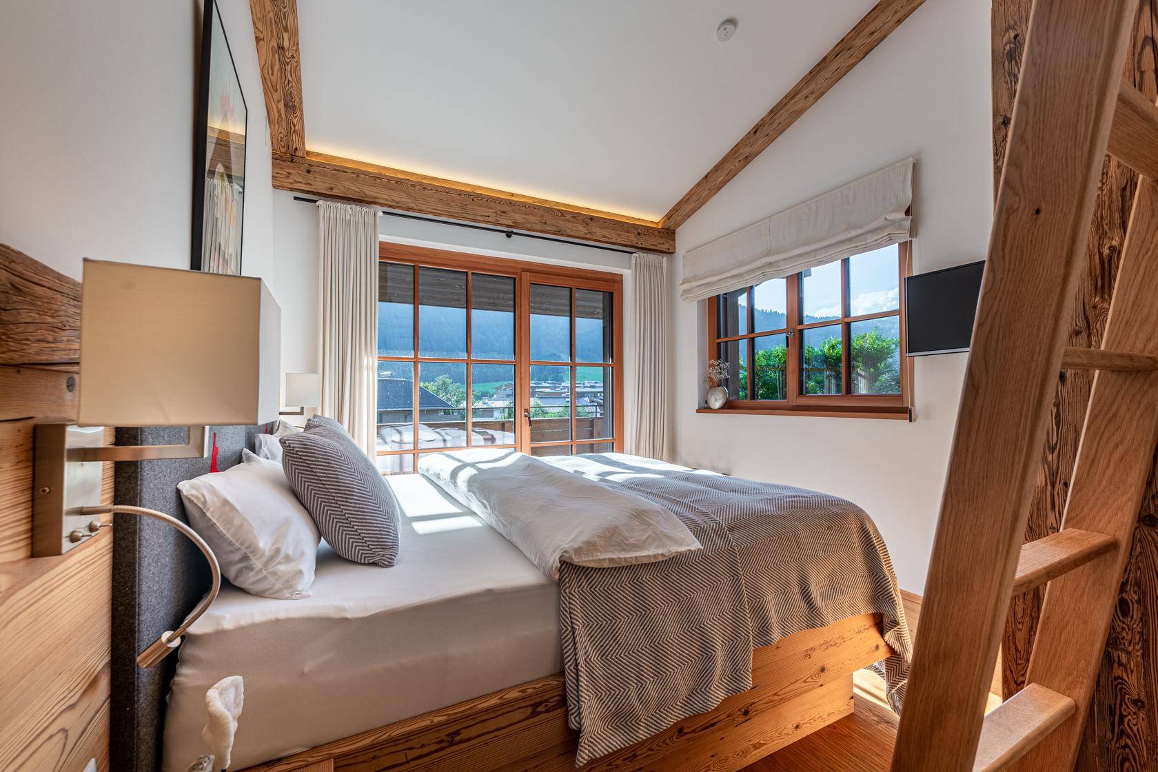 Helles Schlafzimmer mit Holzboden, Balkonzugang und weitem Blick auf die Umgebung.
