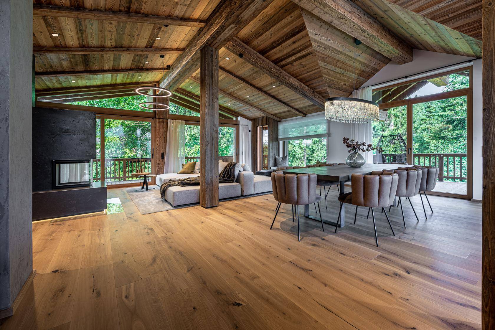 Offener Wohn-Essbereich mit Kamin, Holzbalkendecke und großen Panoramafenstern.