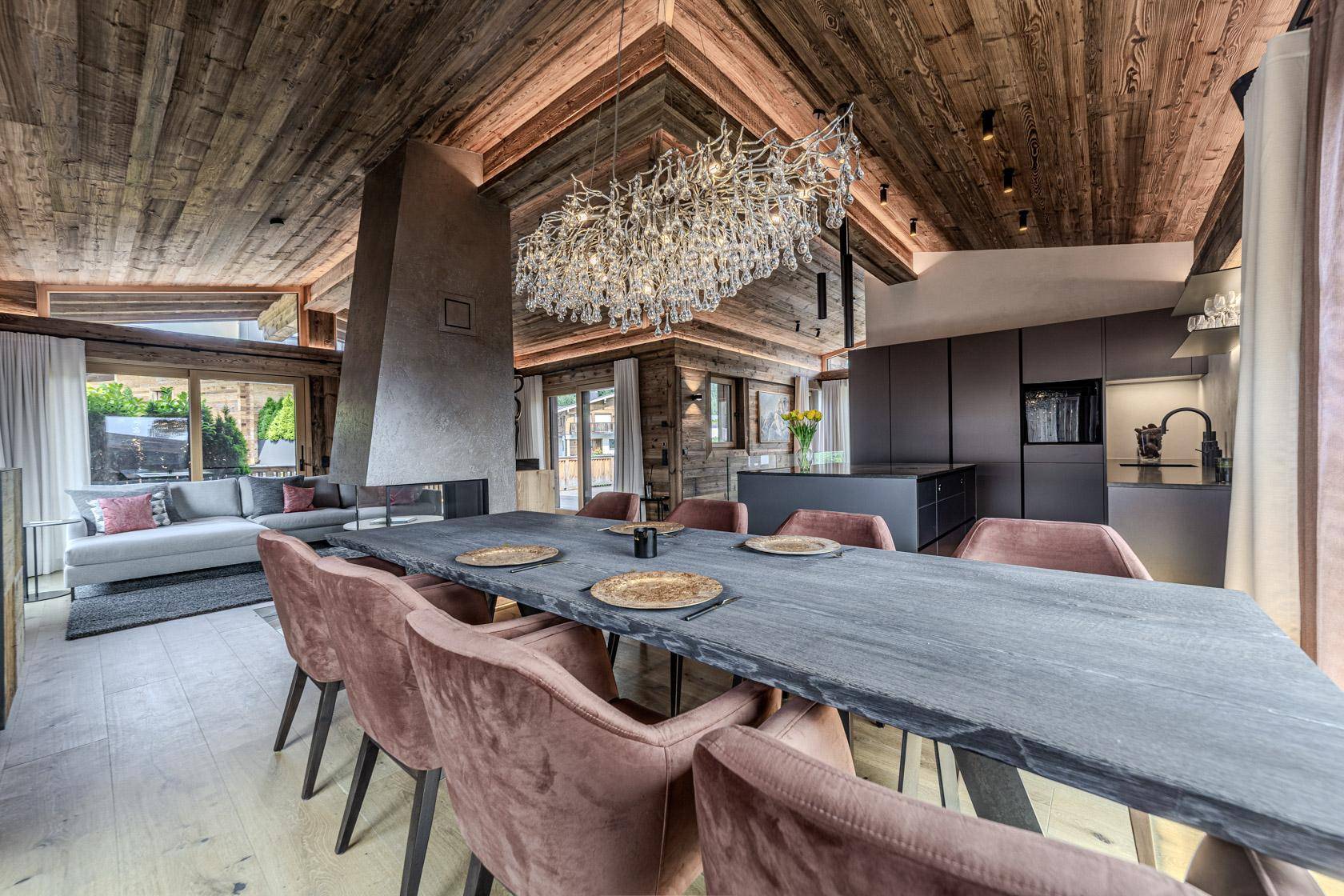 Eleganter Essbereich mit großem Tisch, Samtstühlen und beeindruckendem Kronleuchter unter Holzbalkendecke.