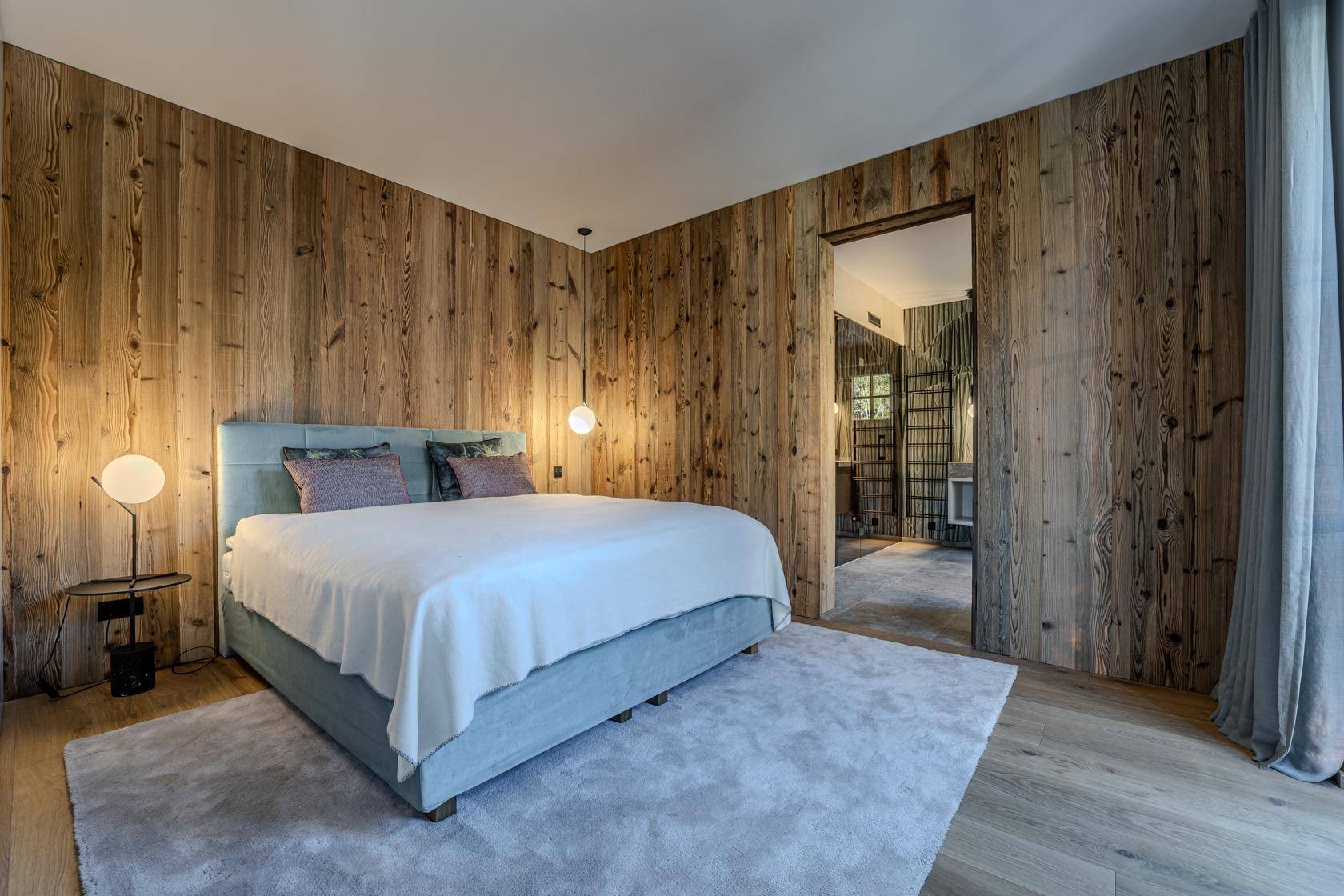 Gemütliches Schlafzimmer mit Holzwänden, Doppelbett und Zugang zu einem weiteren Raum.