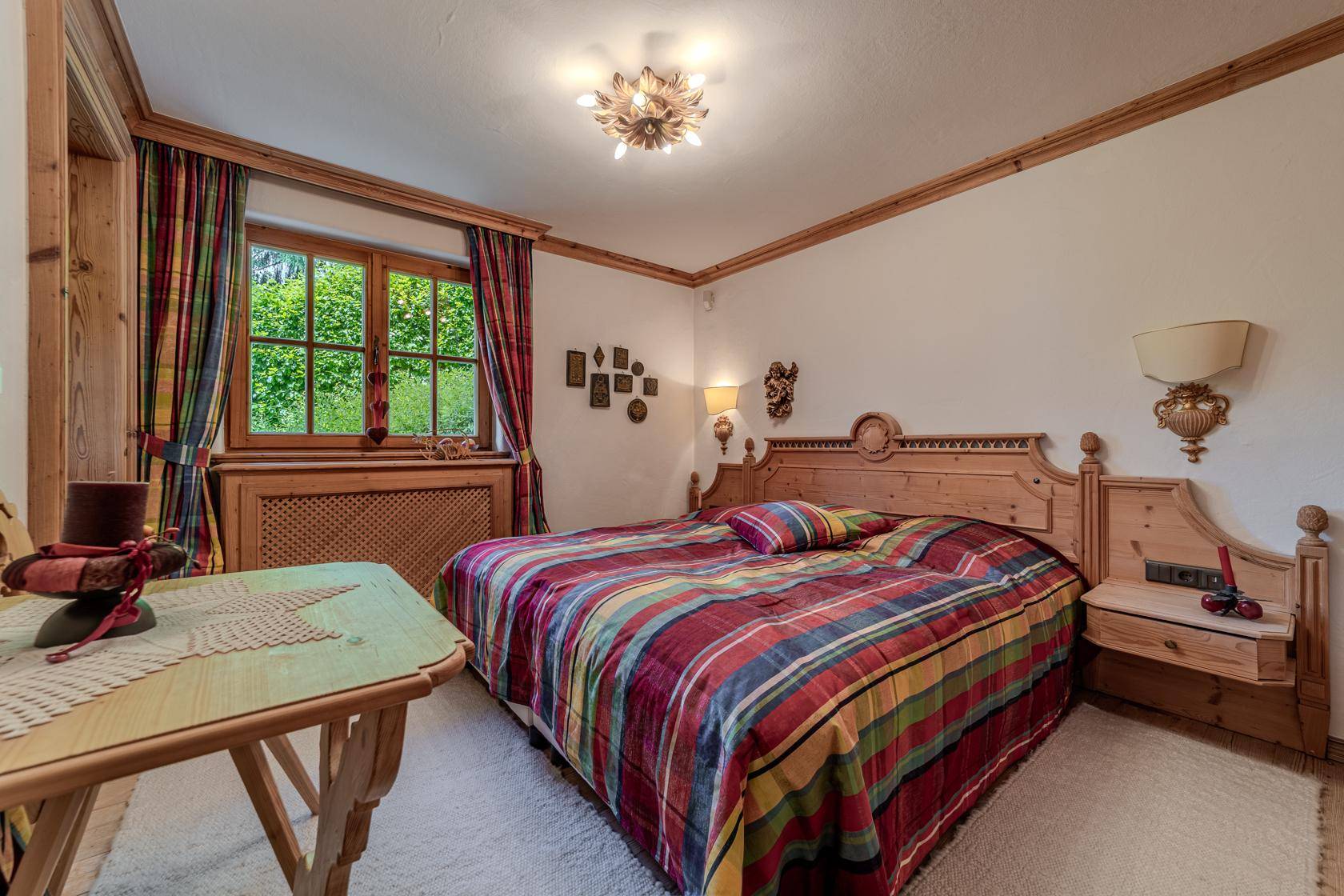 Helles Schlafzimmer mit karierter Bettwäsche, Holzmöbeln und Fenster mit Blick ins Grüne.