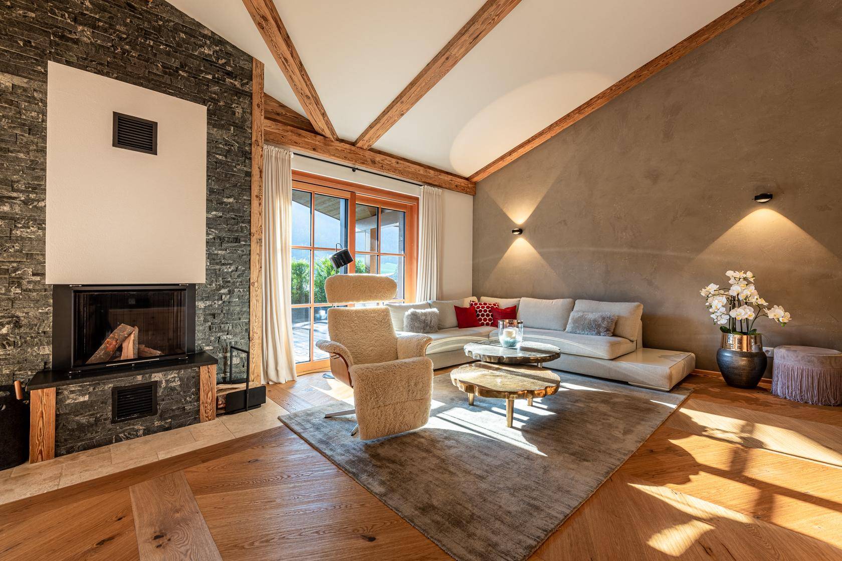 Gemütliches Wohnzimmer mit Kamin, Holzbalken und großen Fenstern für viel Tageslicht.
