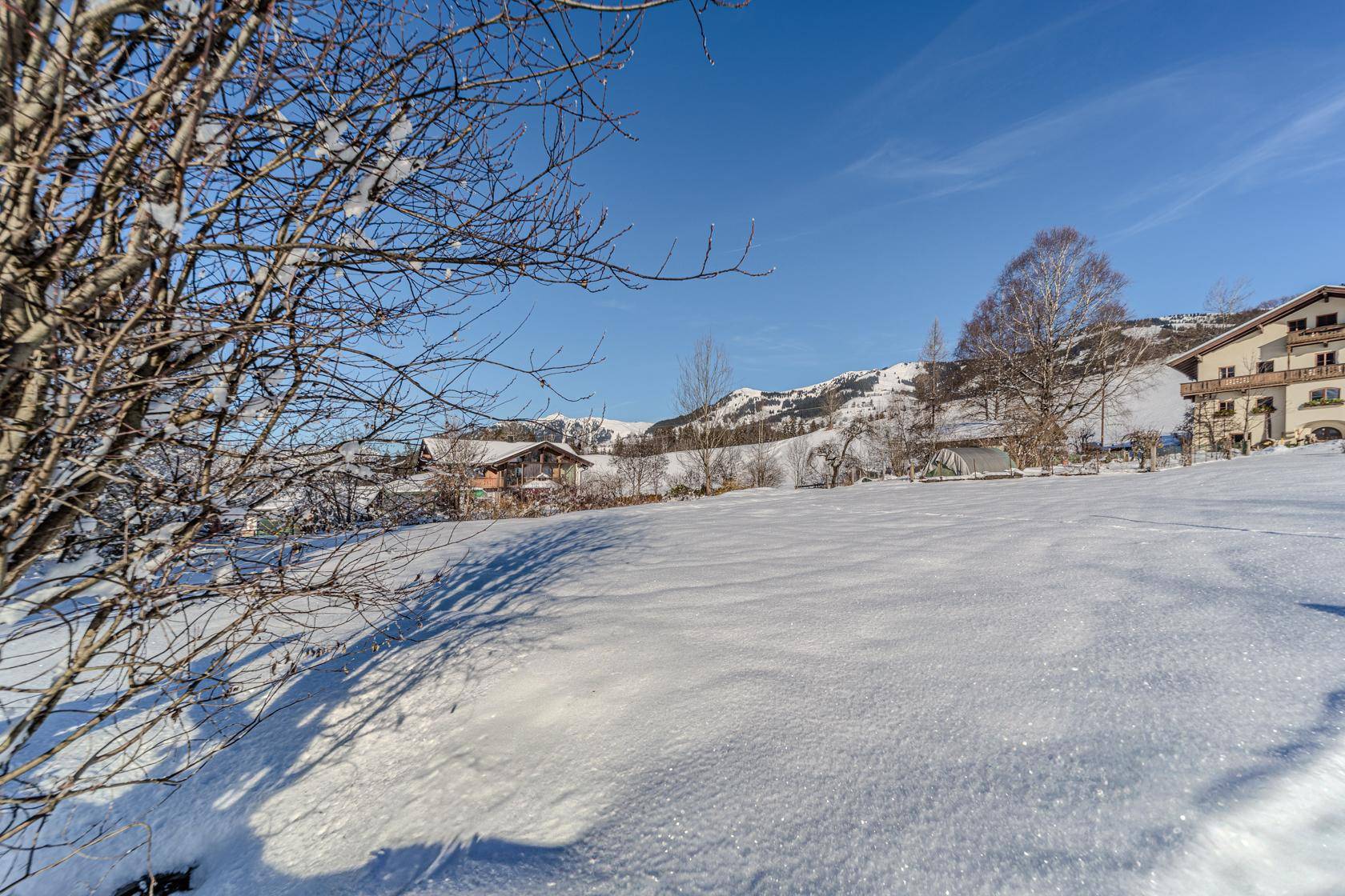 Winterliche Landschaft mit verschneiten Feldern und Bergen unter klarem blauem Himmel.