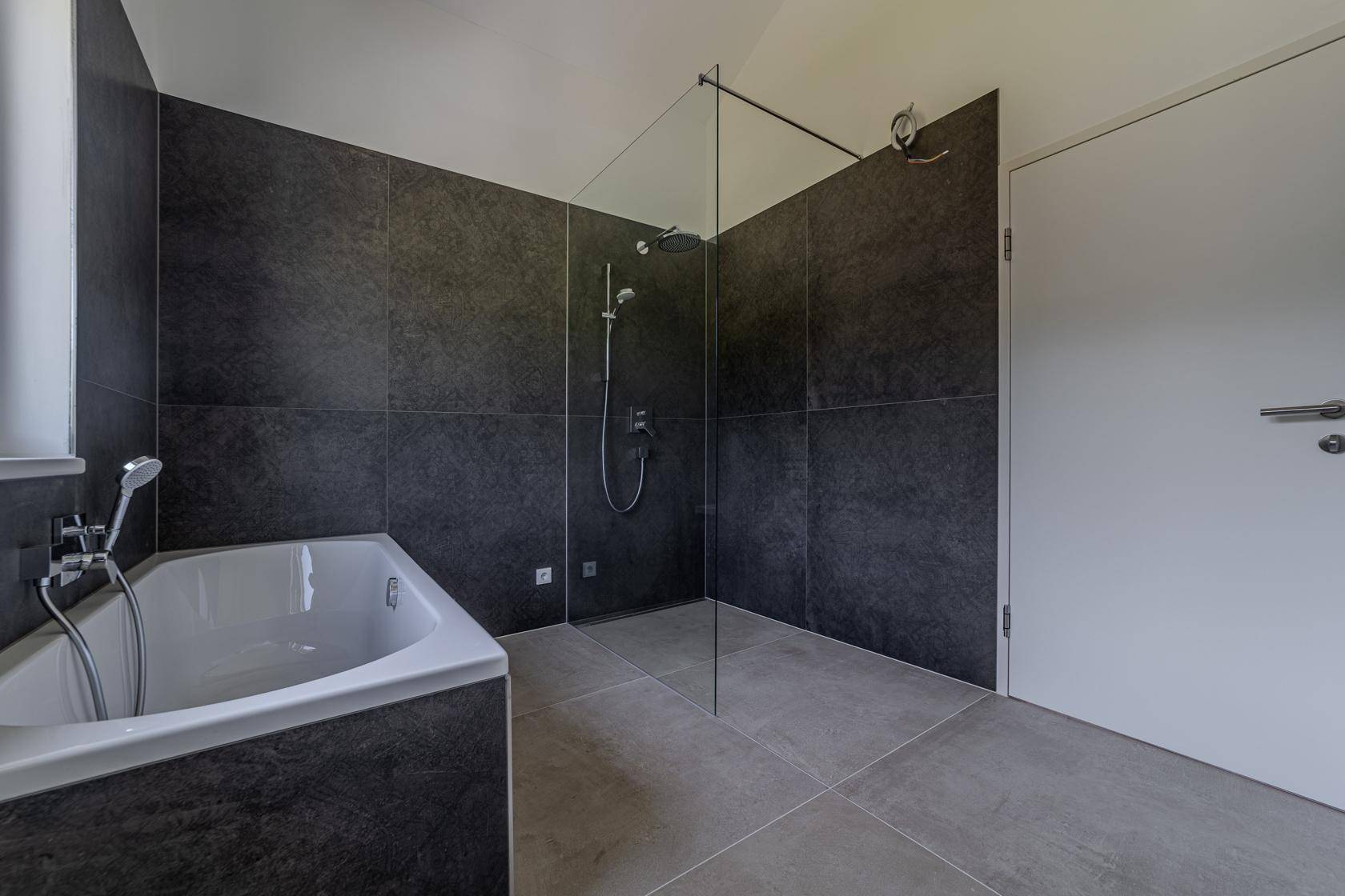 Elegantes Badezimmer mit dunklen Fliesen, Glasduschwand und moderner Regendusche.