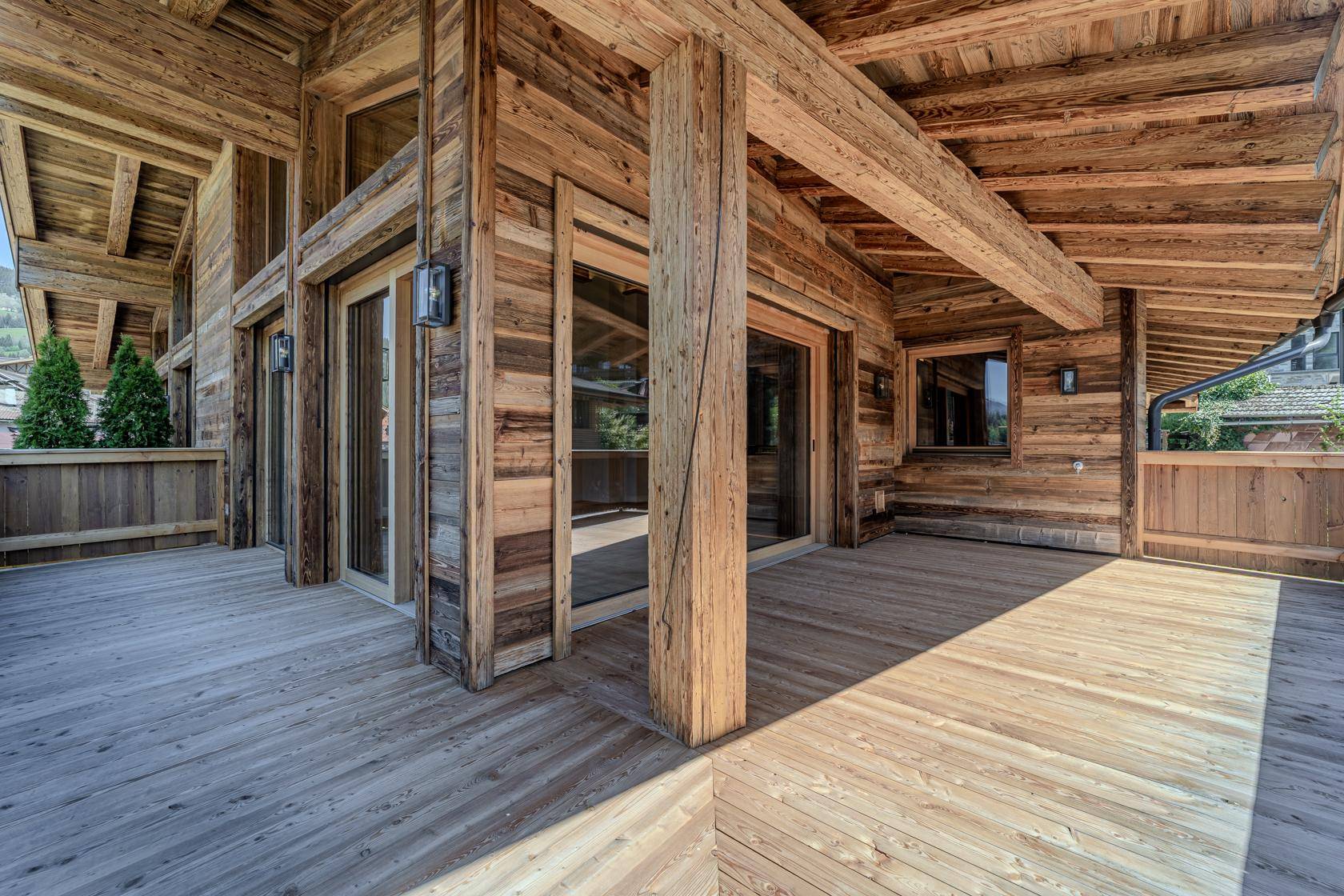 Breite Holzterrasse mit Schiebetüren und einer Fassade aus naturbelassenem Holz, die zum Entspannen einlädt.