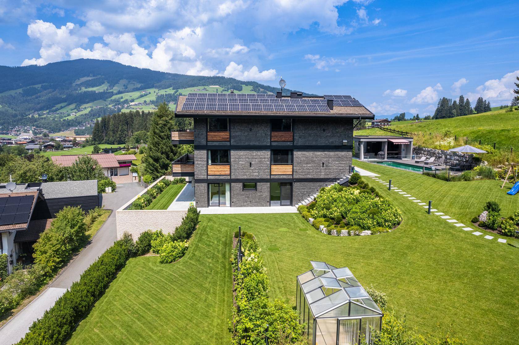Weitläufiges Grundstück mit modernem Haus, gepflegtem Garten, Gewächshaus und Bergblick.