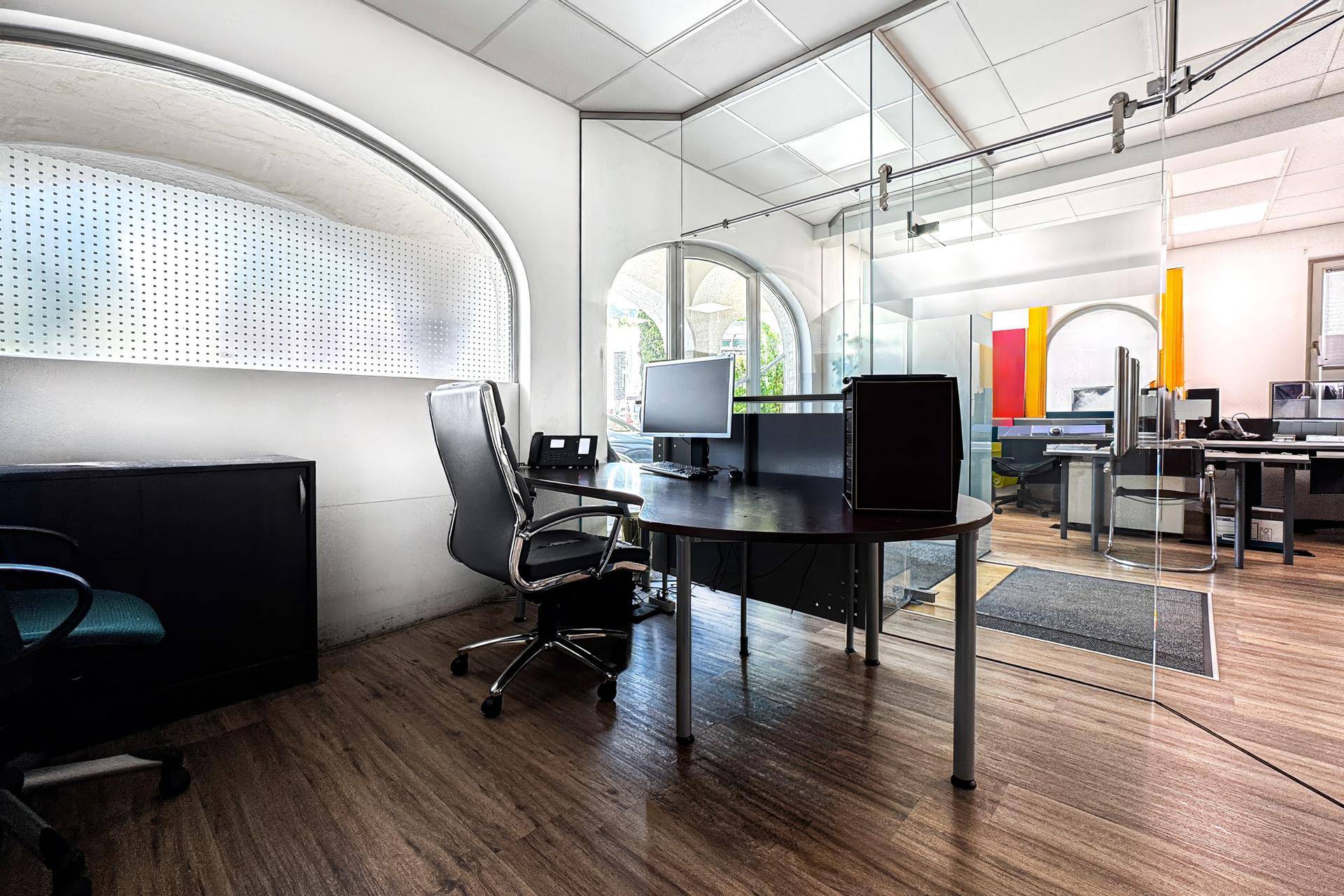 Einzelner Arbeitsplatz in einem modernen Büro mit Holzfußboden und Glasabtrennung.