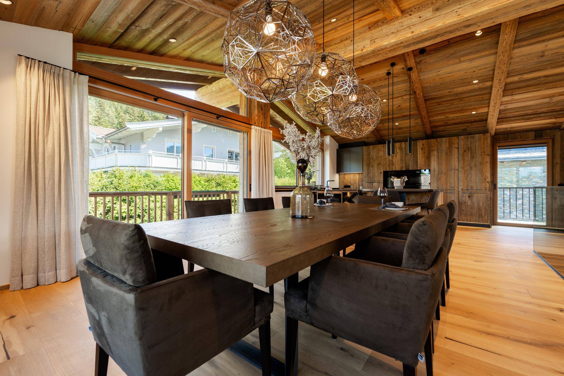 Eleganter Essbereich mit großem Holztisch, modernen Leuchten und Panoramablick auf die Berge.