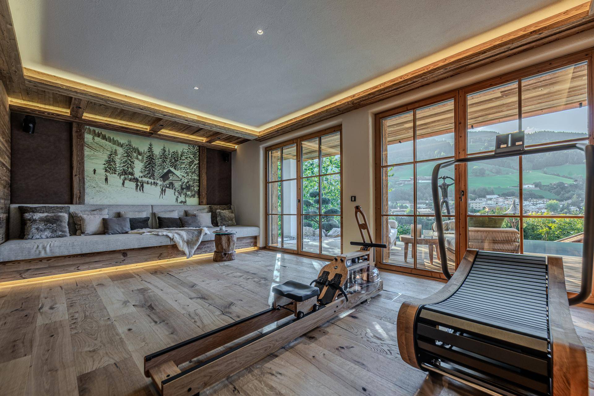 Heller Fitnessraum mit großen Fenstern, Holzboden und Blick auf die grüne Landschaft.