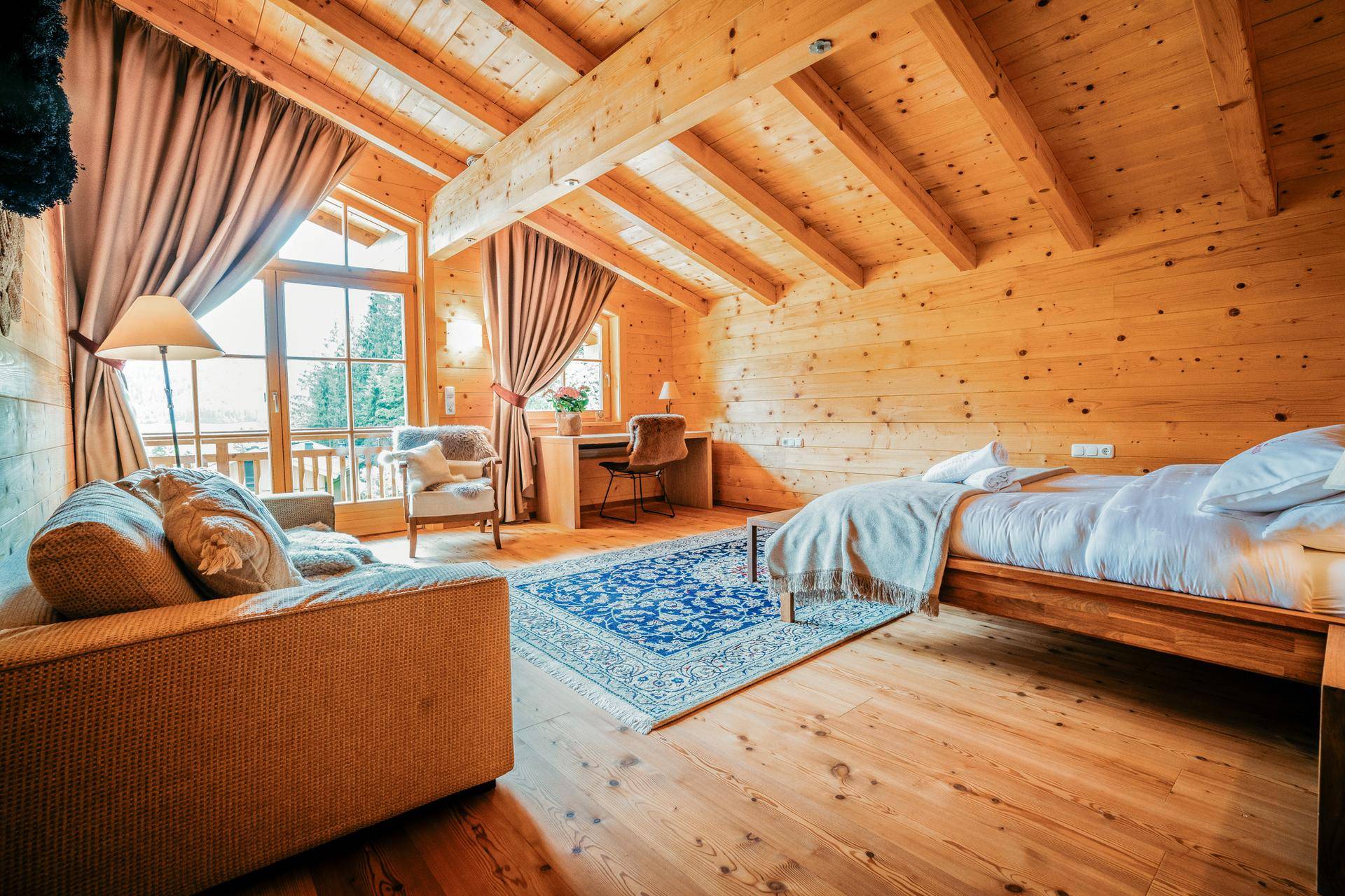 Helles Schlafzimmer mit Holzboden, Holzwänden, Dachschrägen und Zugang zu einem Balkon mit Bergblick.