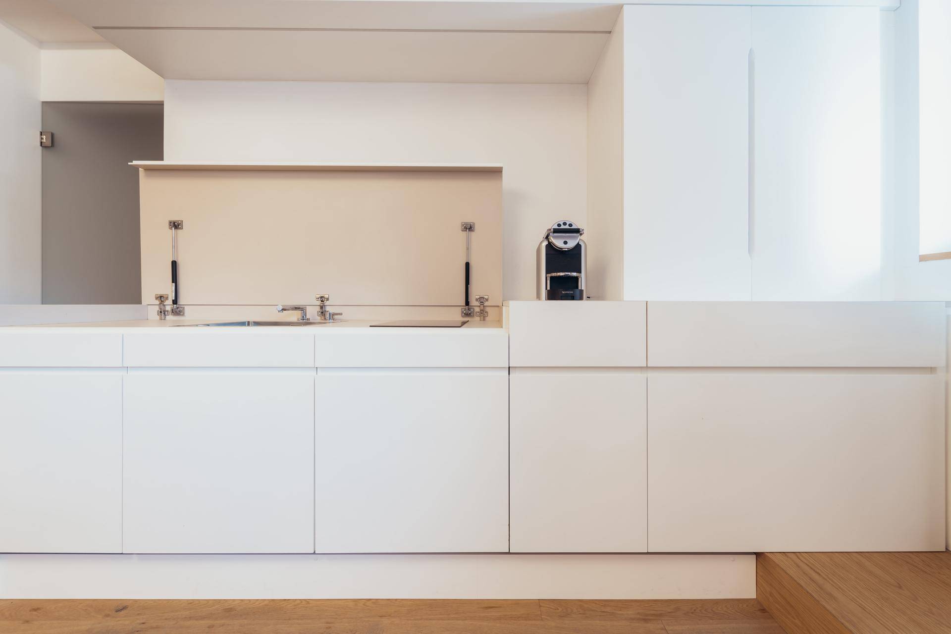 Moderne, weiße Küchenzeile mit integriertem Spülbecken und Kaffeemaschine in minimalistischem Design.