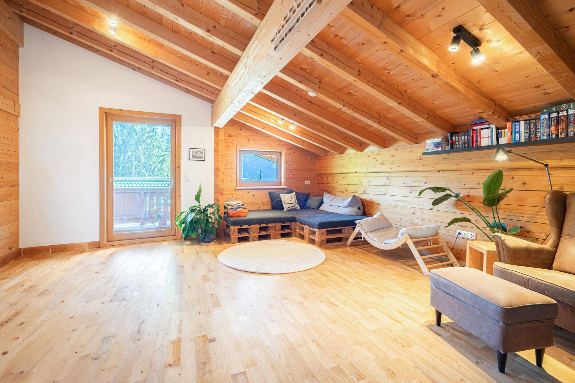 Helles Wohnzimmer mit Holzbalkendecke, Zugang zum Balkon und moderner Paletten-Sitzgruppe.