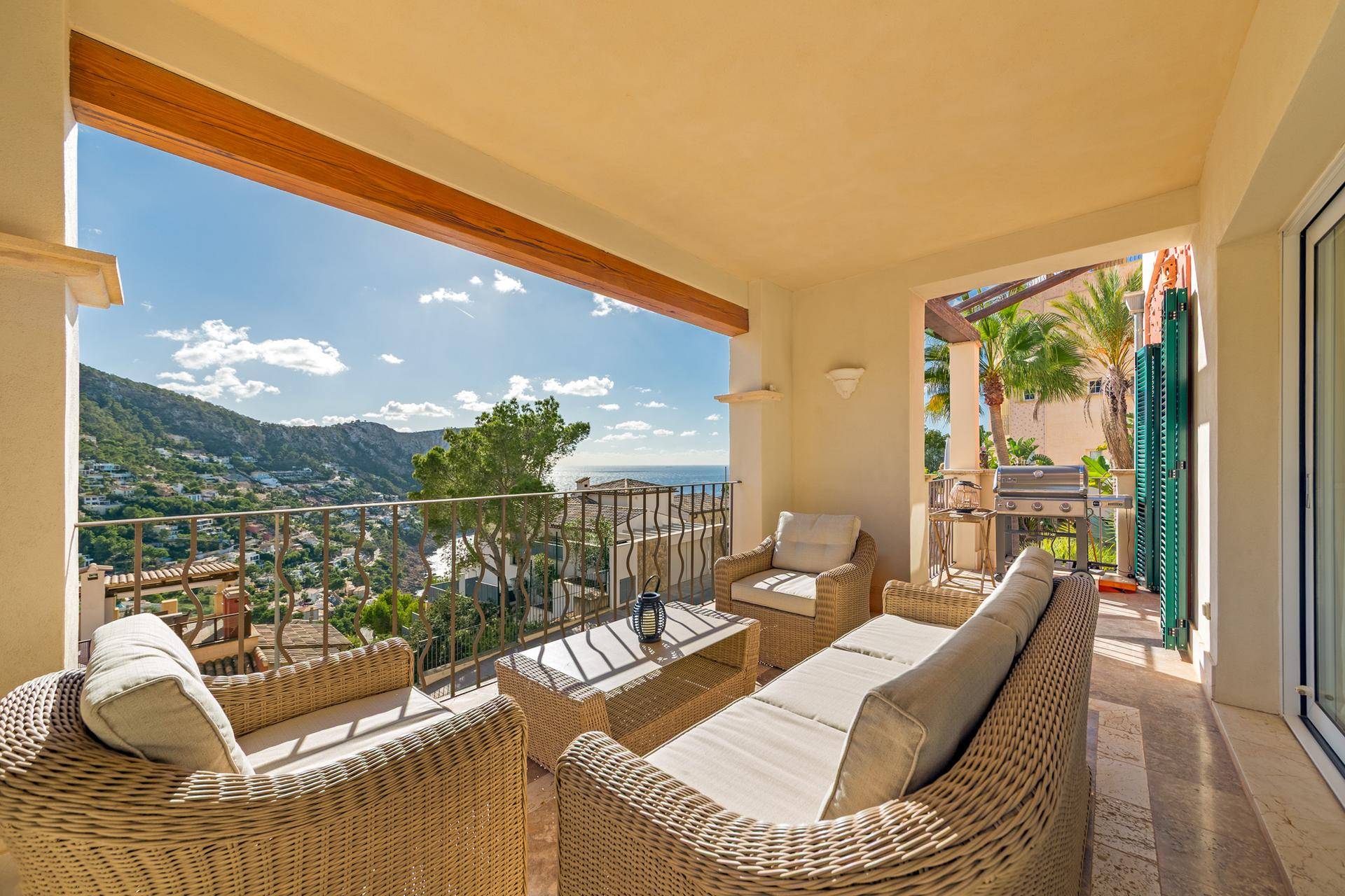 Geräumiger Balkon mit Korbmöbeln, Grill und weitem Blick auf das Meer und die Berge.